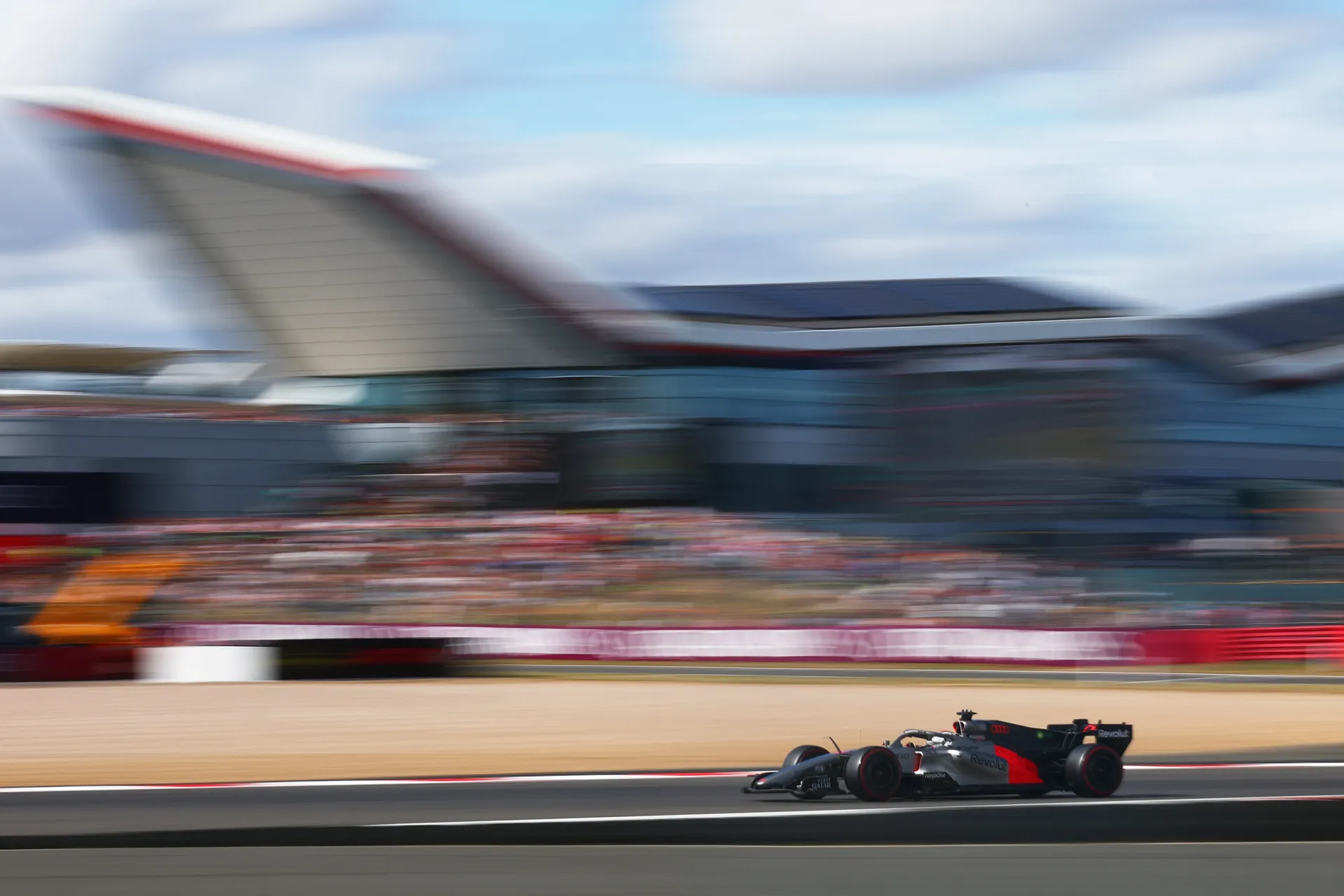 Audi Revolut F1® Team car driven by Gabriel Bortoleto in a long panning shot at Silverstone with blurred grandstands emphasising speed.