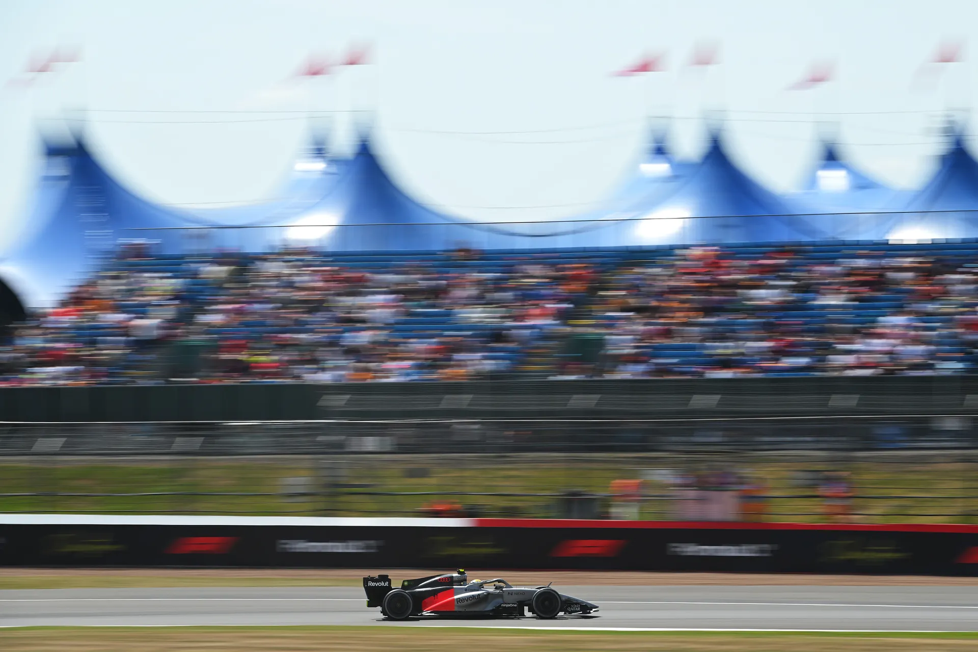 The Audi R26 speeds past packed grandstands at Silverstone with fans blurred in motion.