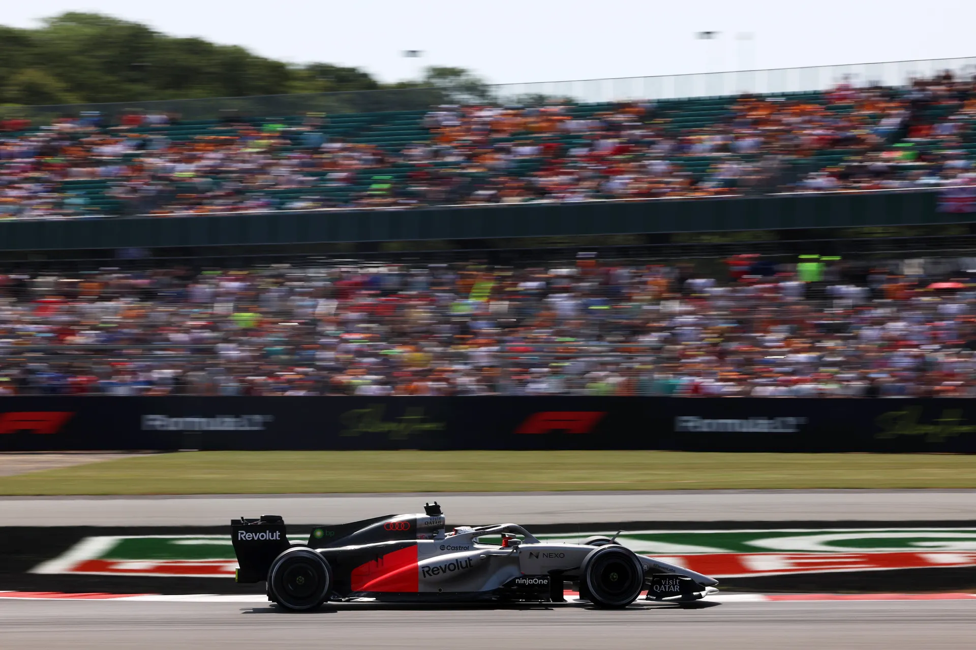 The Audi R26 speeds past packed grandstands at Silverstone with fans blurred in motion.
