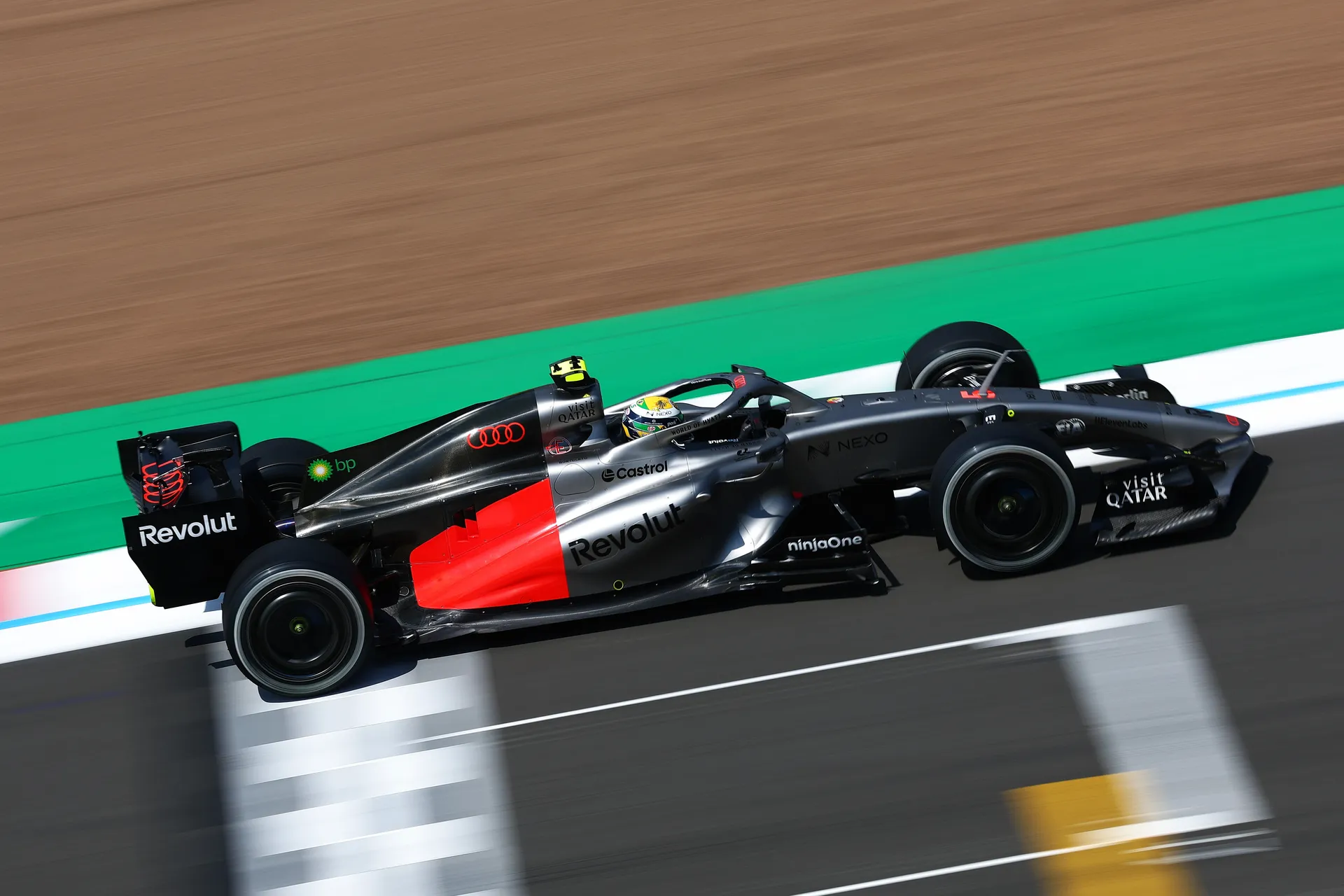 The Audi R26 runs at speed along the circuit with green runoff areas beside the track.