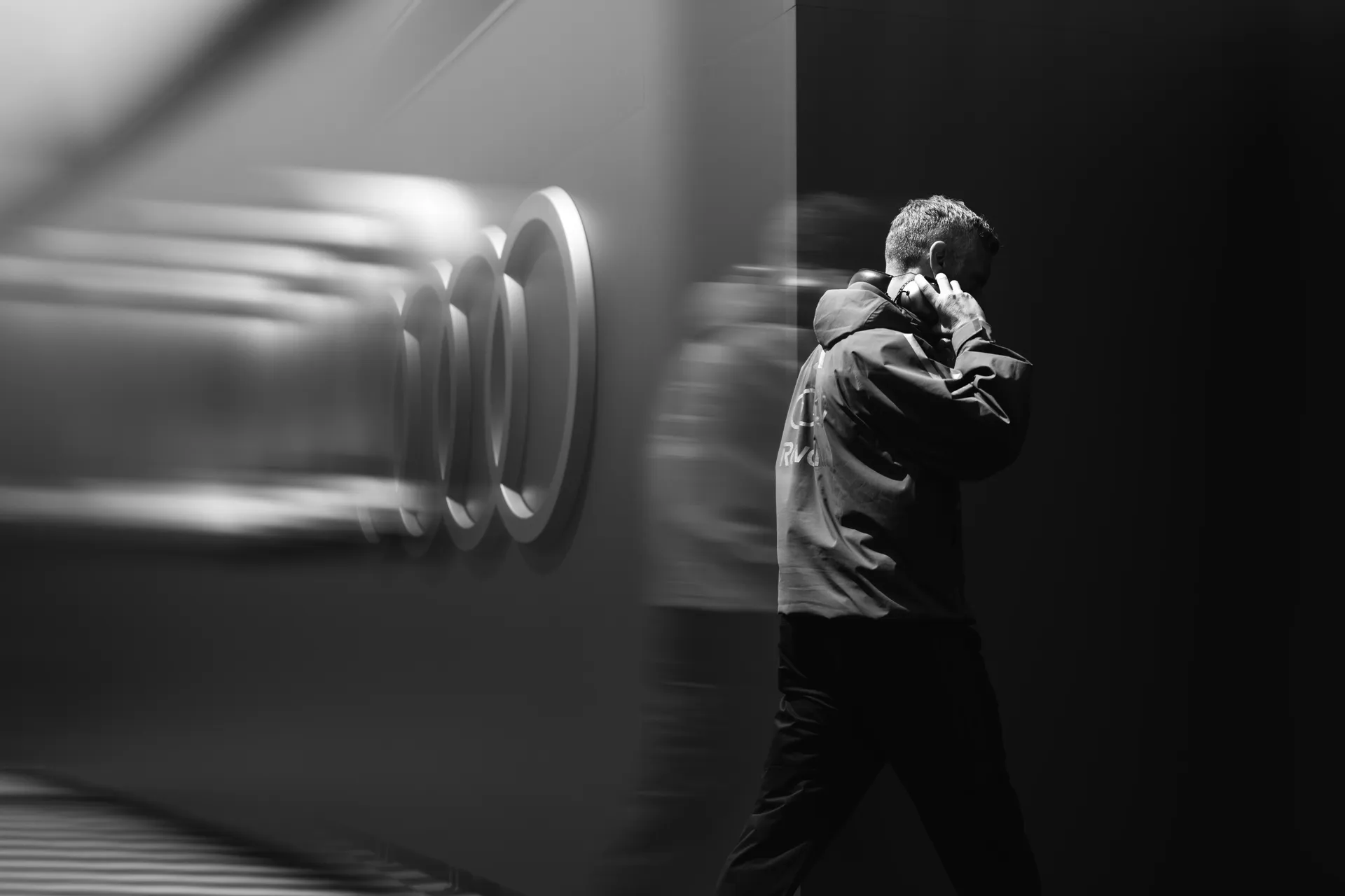 A member of the Audi Revolut F1® Team walks past Audi branding in a black-and-white paddock shot.
