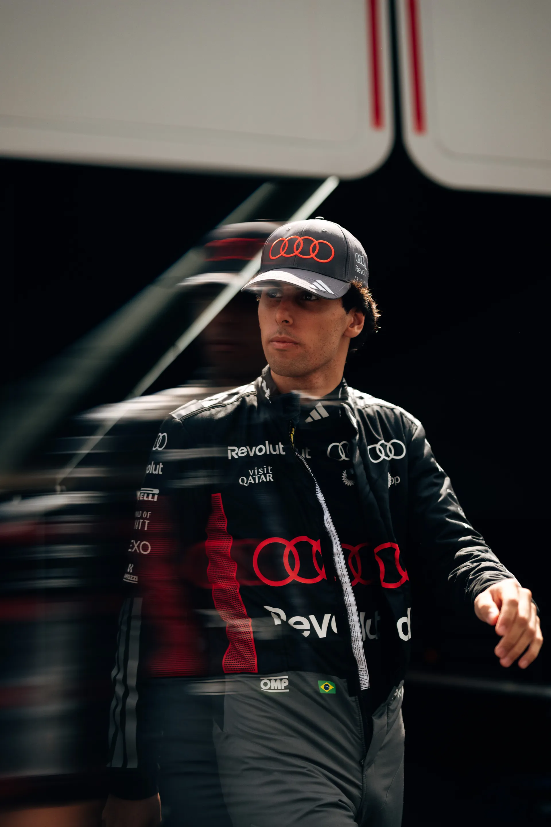 Gabriel Bortoleto walks through the paddock in Audi Revolut F1® Team race gear, framed by motion blur.