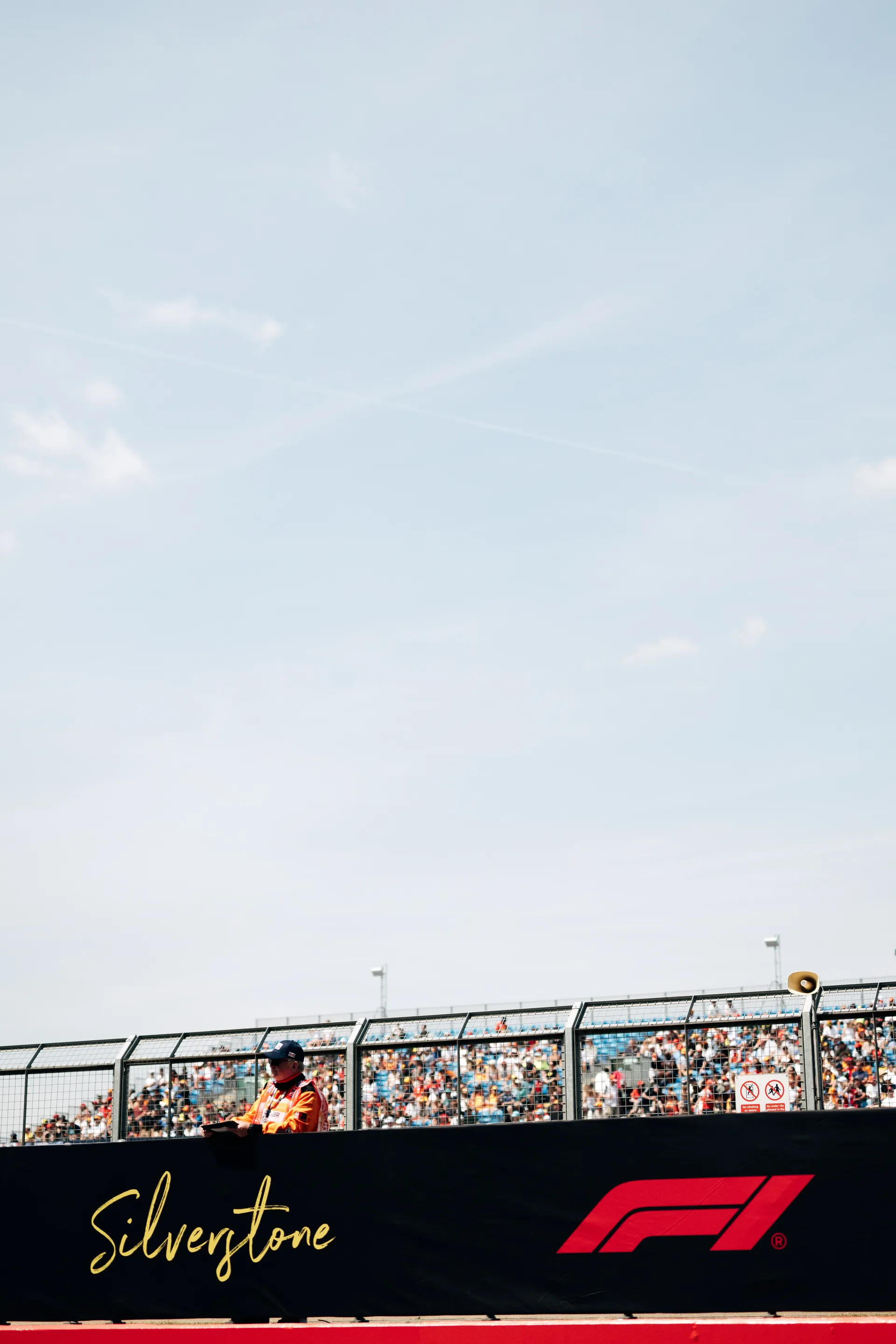 Silverstone trackside barrier with Formula 1 branding and fans in the grandstand behind.