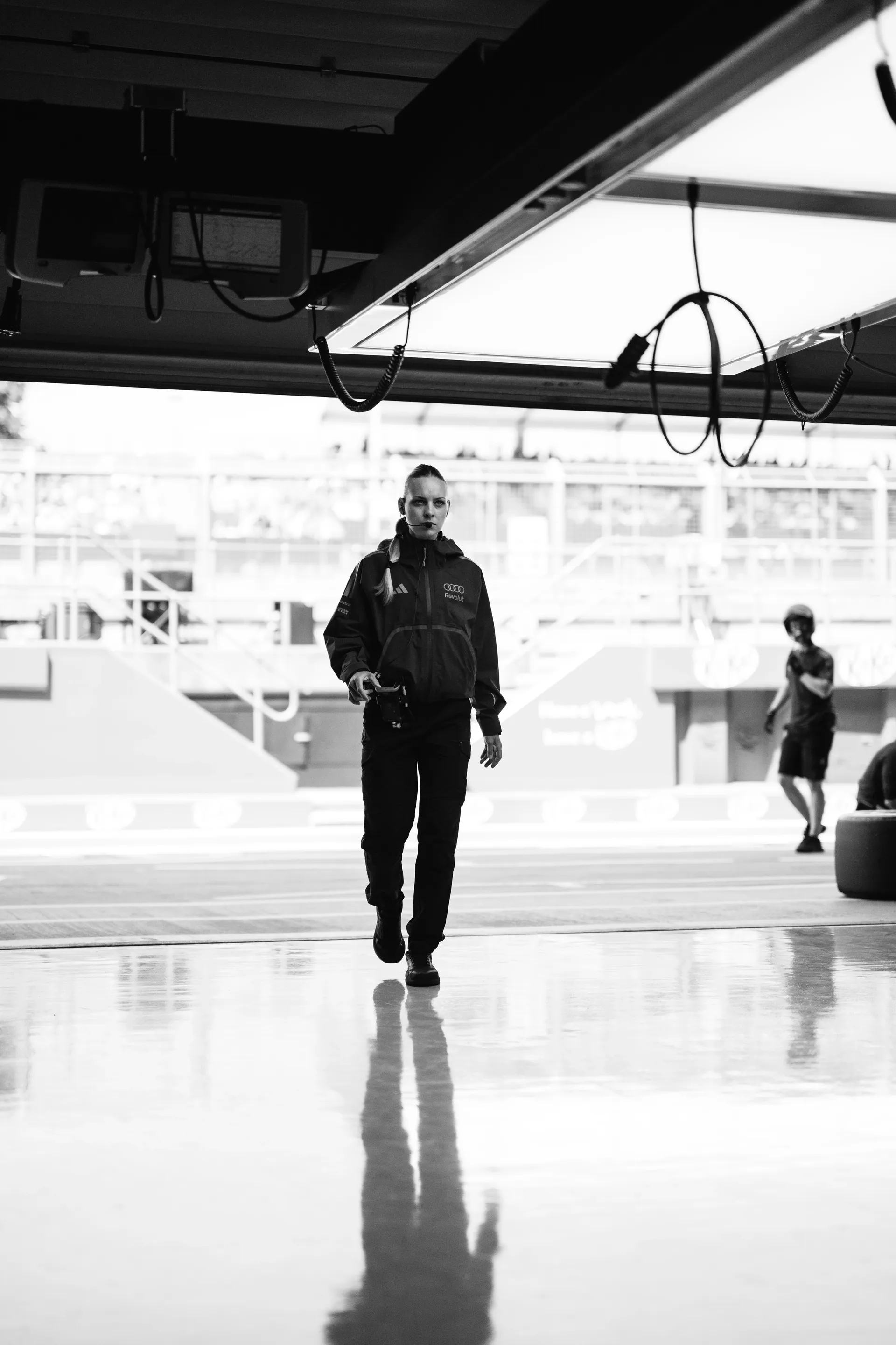 A member of the Audi Revolut F1® Team walks through the garage in a black-and-white shot with strong reflections.