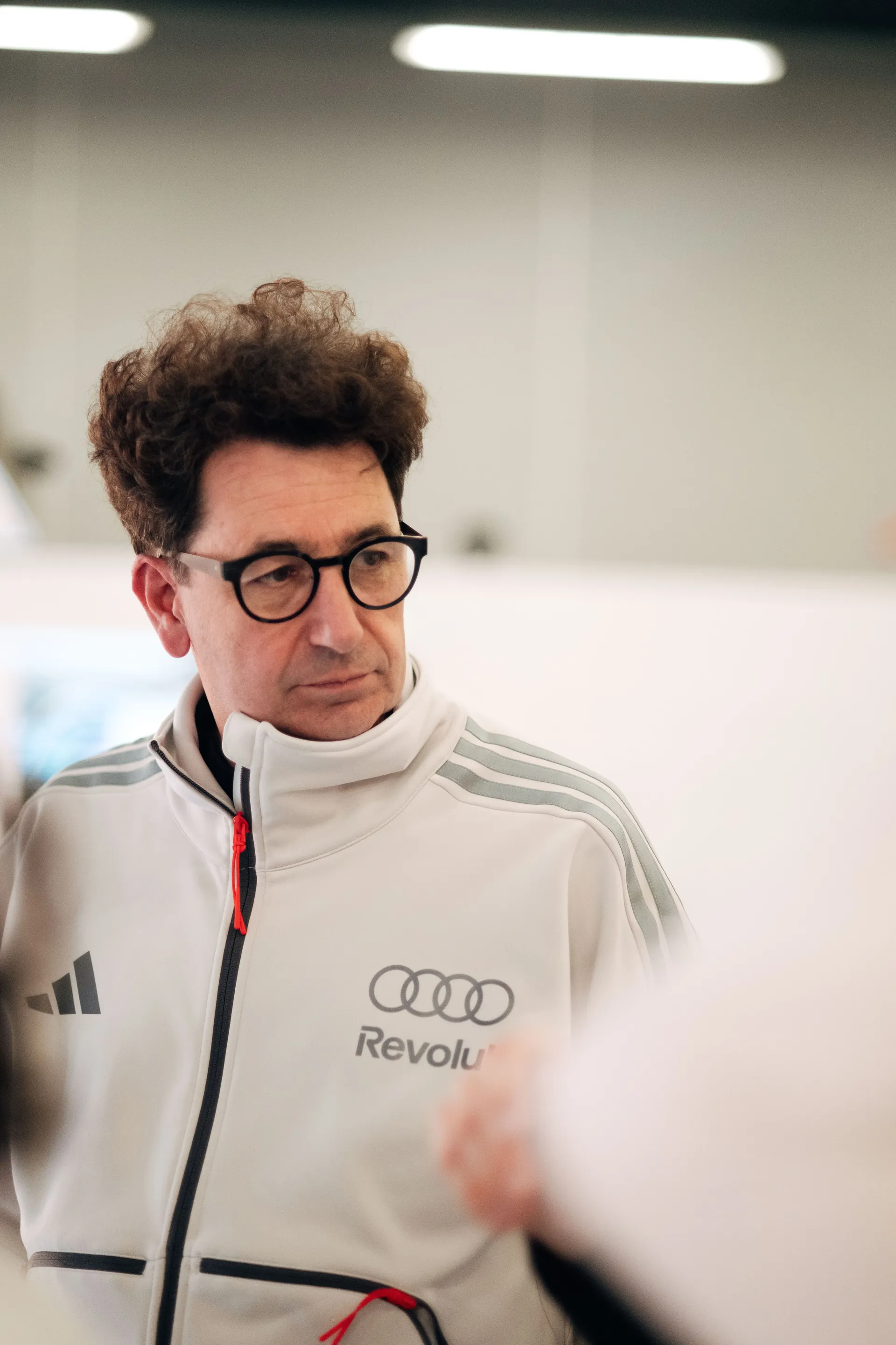 Close-up of Mattia Binotto in Audi Revolut F1® Team apparel observing activity inside the garage.
