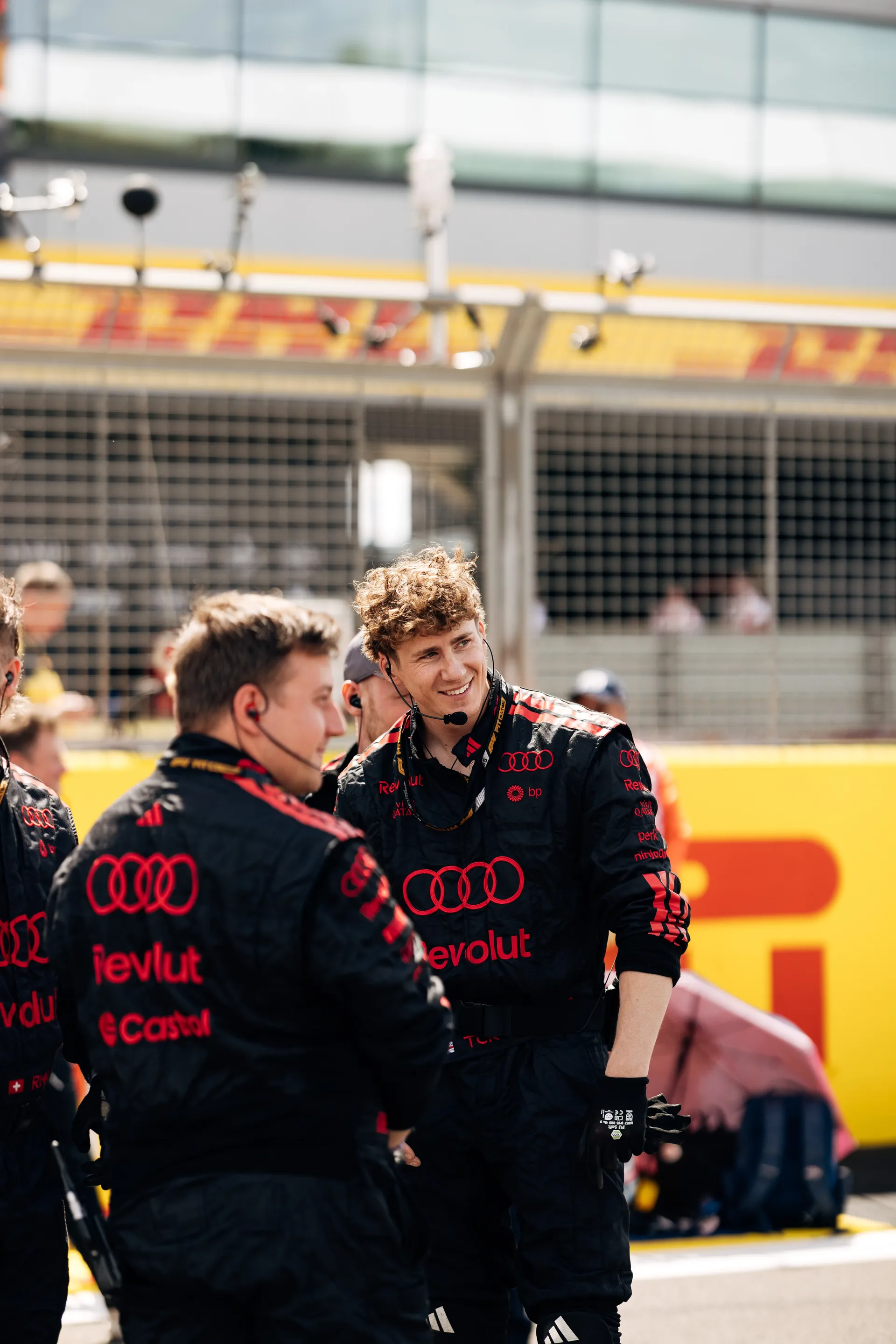 Audi Revolut F1® Team crew members stand on the grid in race suits, communicating and preparing for the Sprint race at Silverstone.