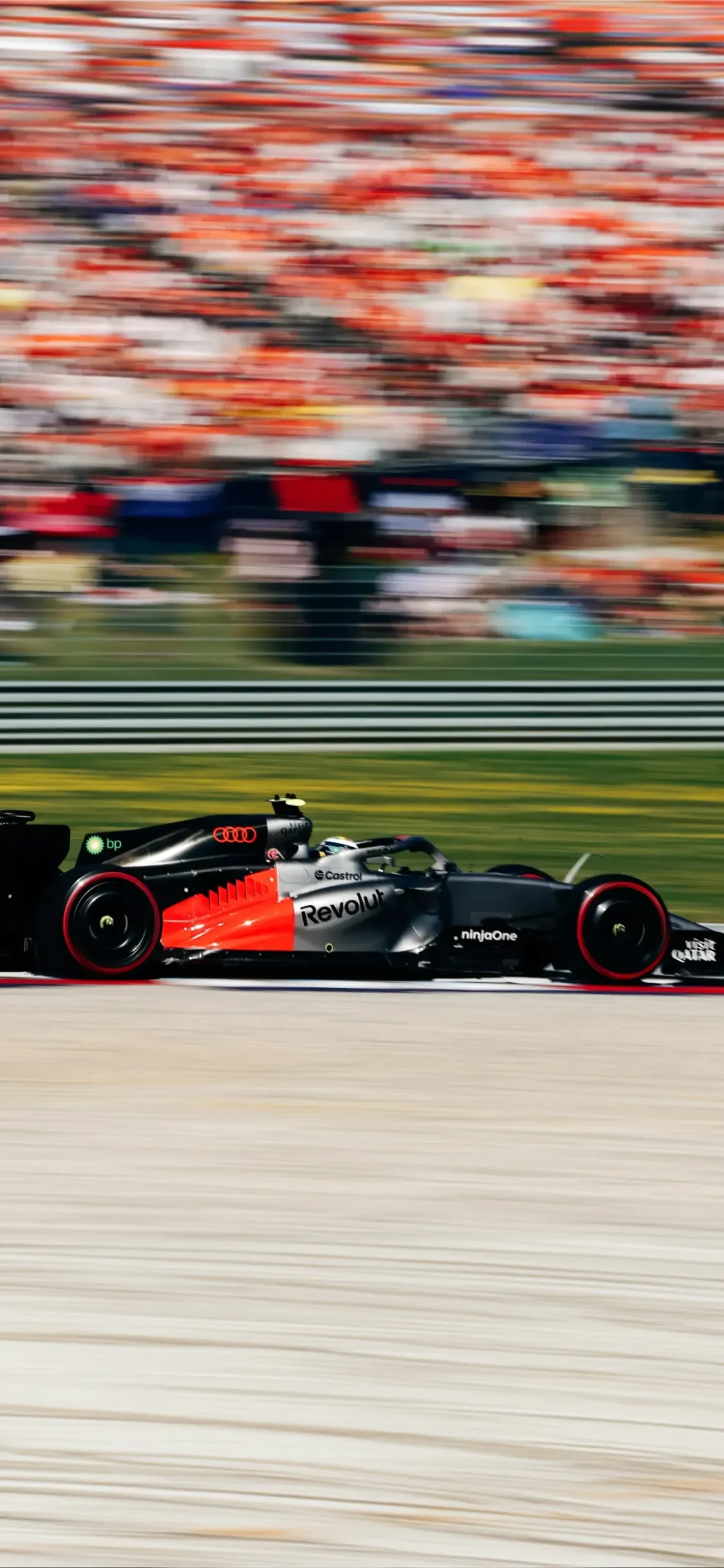 Audi Revolut F1® Team car at speed on track, captured in motion blur with packed grandstands in the background, emphasizing pace and intensity.