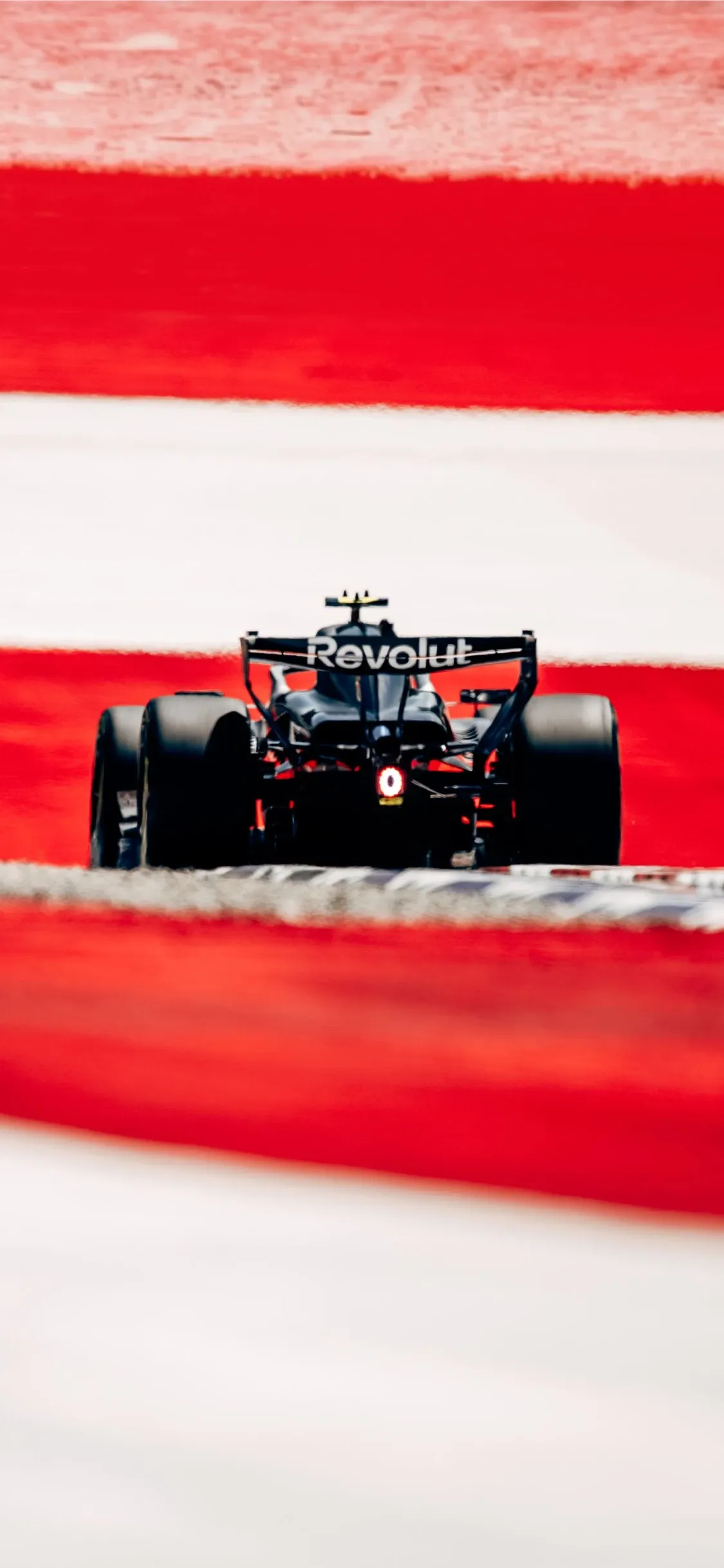 Rear view of the Audi Revolut F1® Team car driving across the red and white kerbs of the Red Bull Ring, highlighting the distinctive Spielberg track colours.