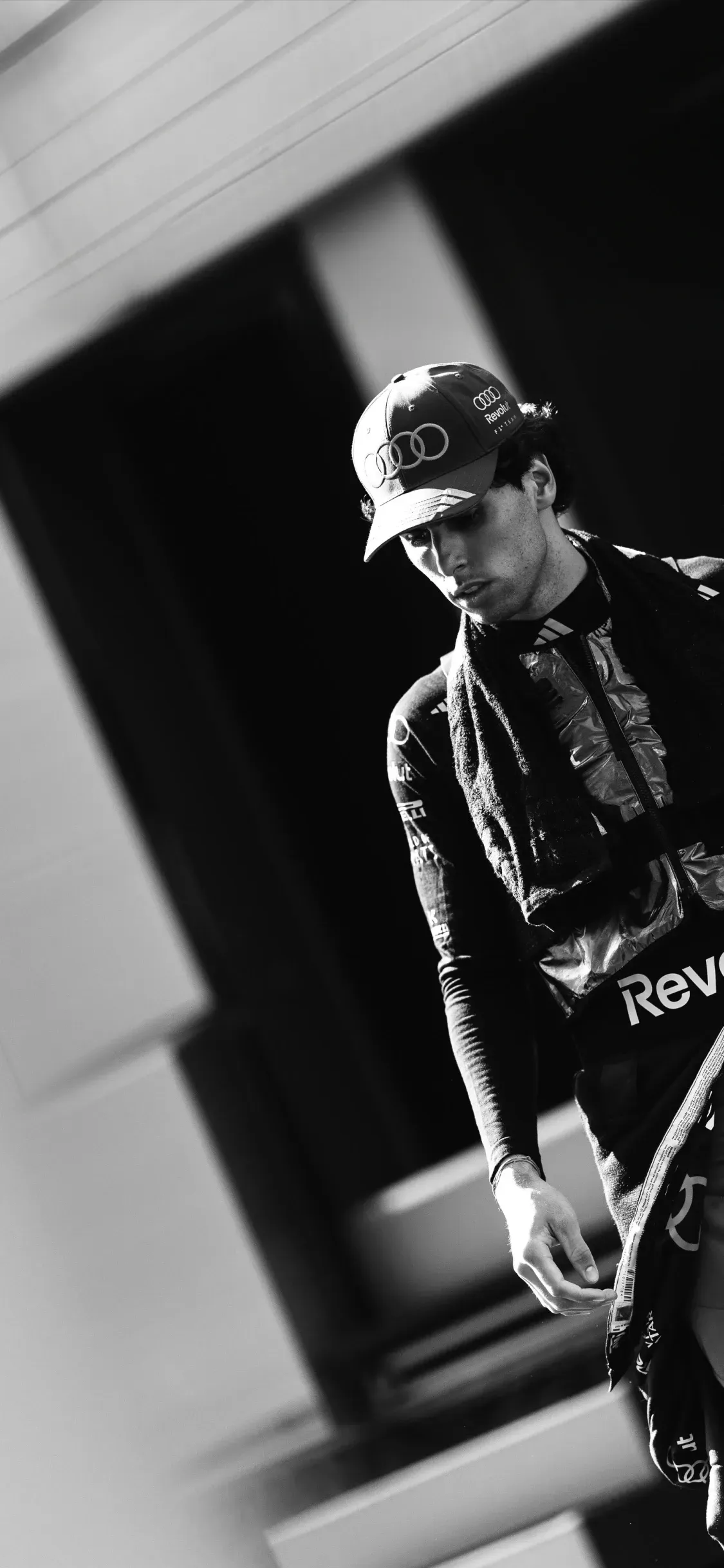Black and white portrait of an Audi Revolut F1® Team driver Gabriel Bortoleto in team kit, looking down in a quiet moment of focus before track action.