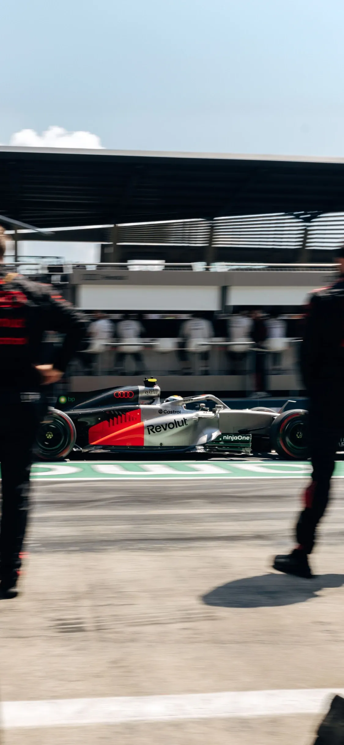 Audi Revolut F1® Team car passing through the pit lane as team members move alongside, capturing the rhythm and coordination of race operations.