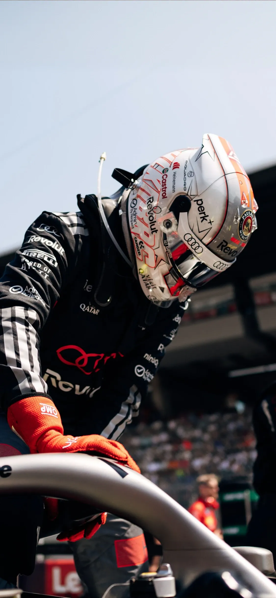 Audi Revolut F1® Team driver Nico Hulkenberg leaning over the cockpit during a pit stop moment, hands positioned on the halo, fully focused on the car.