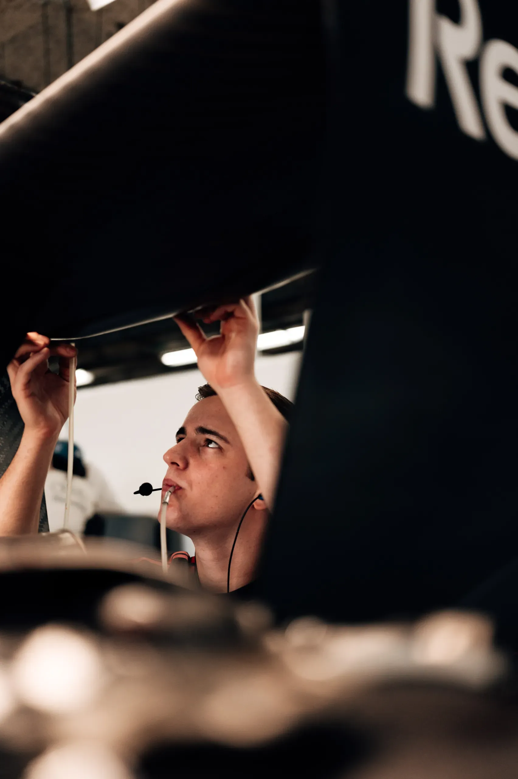 A mechanic of the Audi Revolut F1® Team with a headset reaching up to work on the Audi R26 in the garage