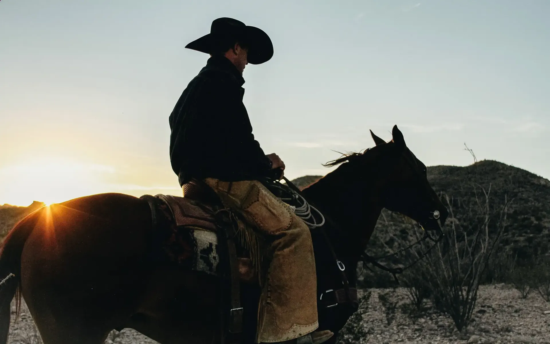 Cowboy riding a horse across the Texas landscape at sunset.