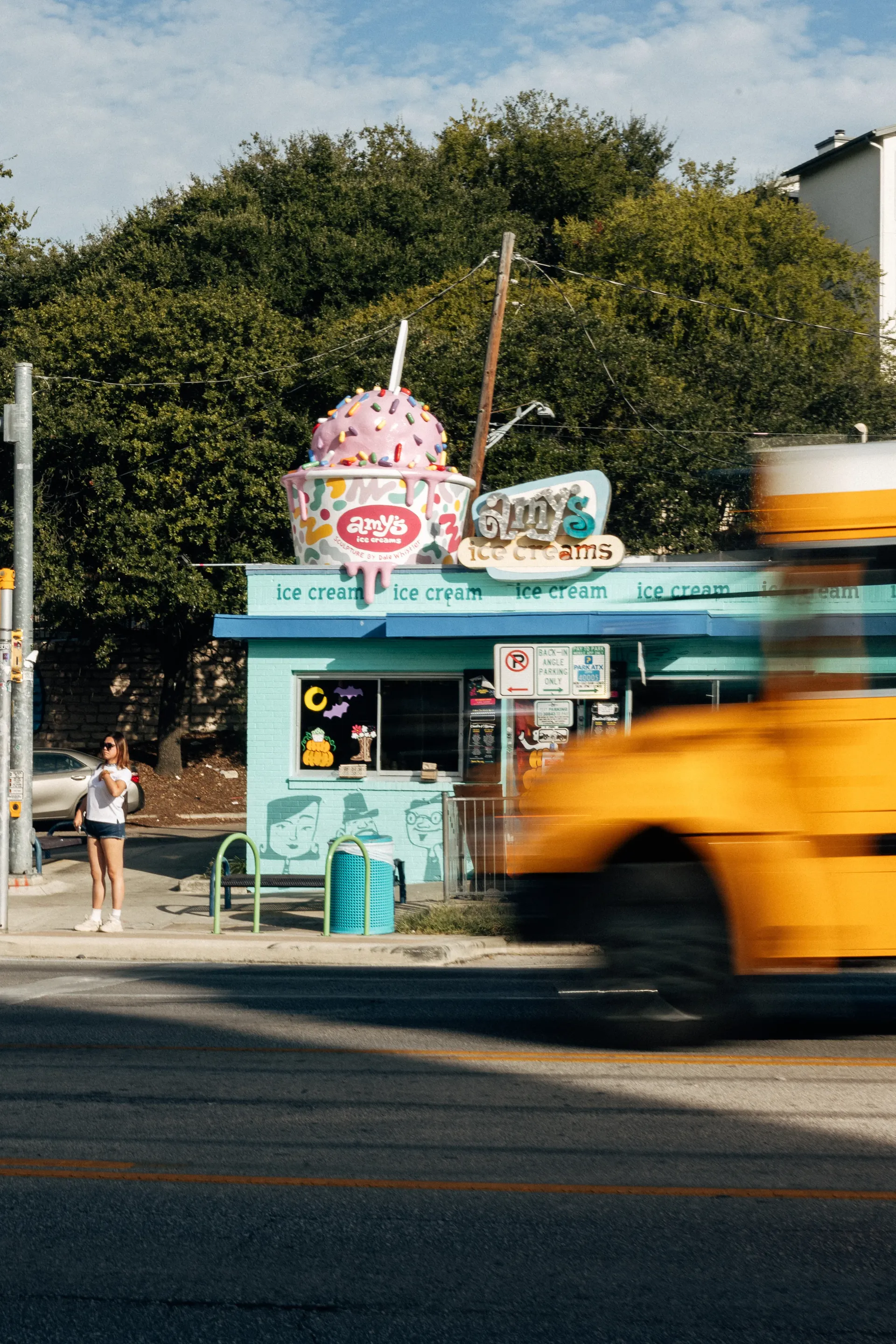 Amy’s Ice Creams shop with a giant ice cream cup sculpture as a yellow school bus passes in Austin
