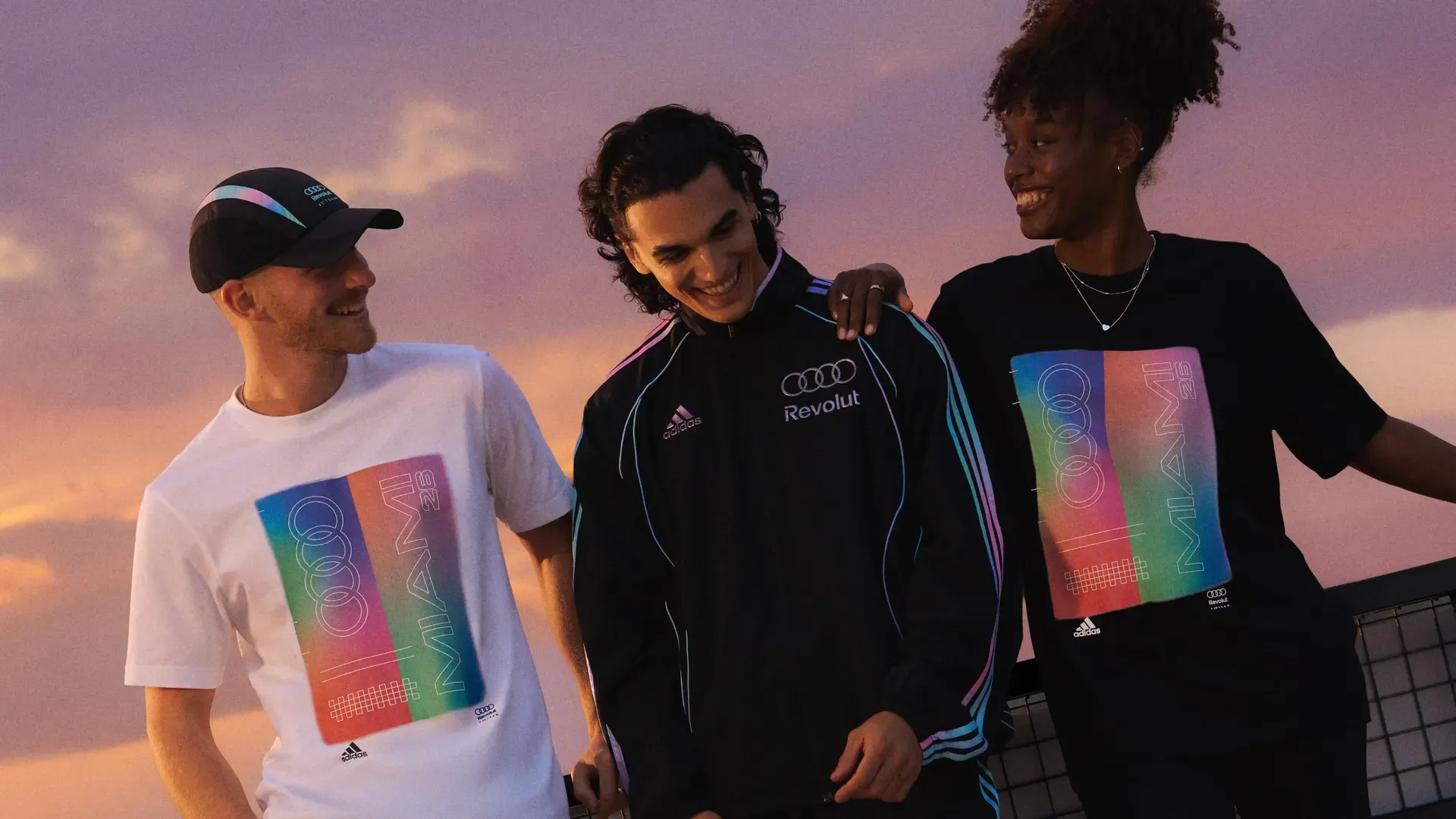 Relaxed group of three young male and female models standing together in a studio with a sunset-style background, wearing casual adidas Miami fanwear outfits