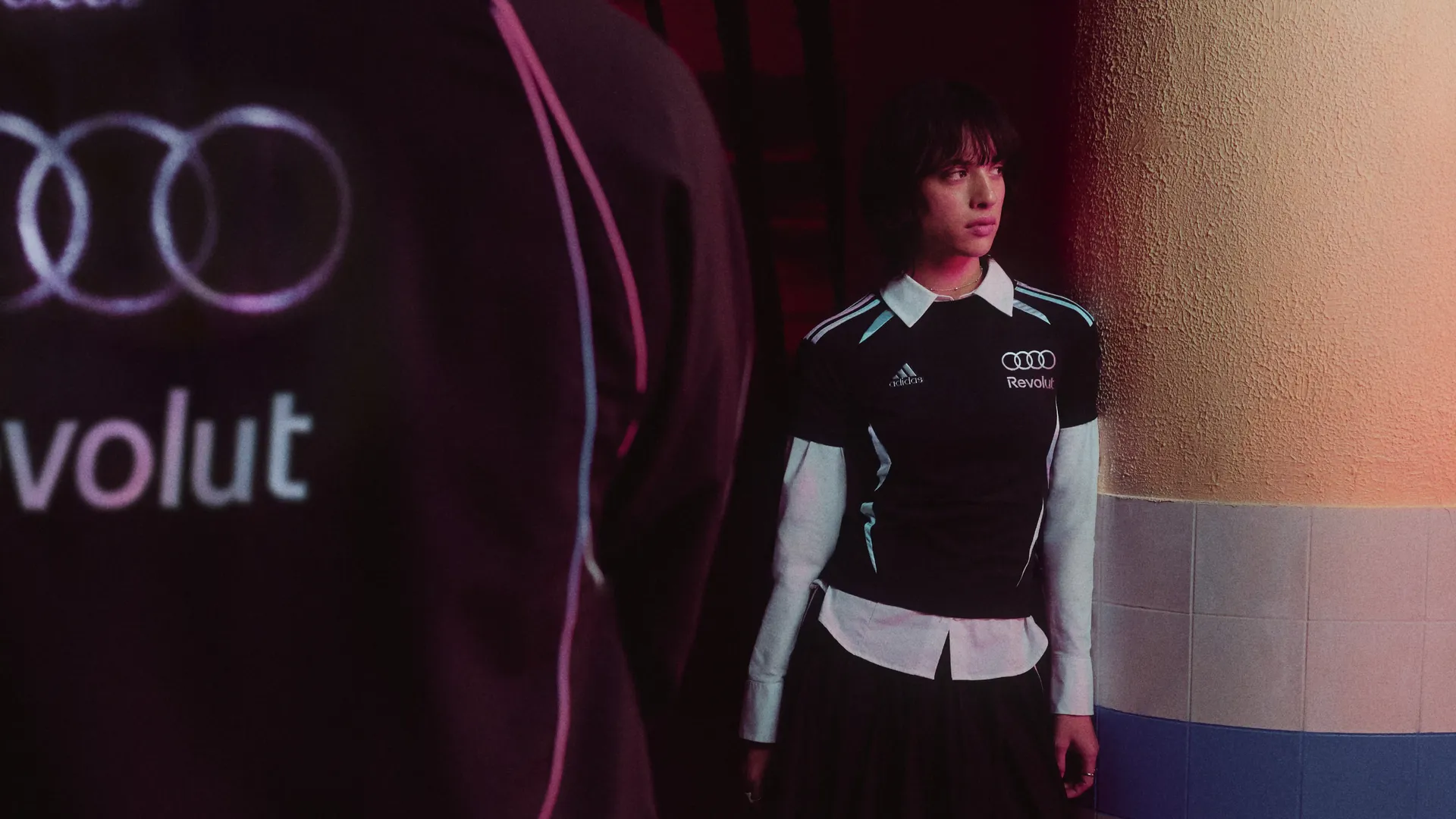 Young female model leaning against the wall wearign black adidas teamwear outfit in studio