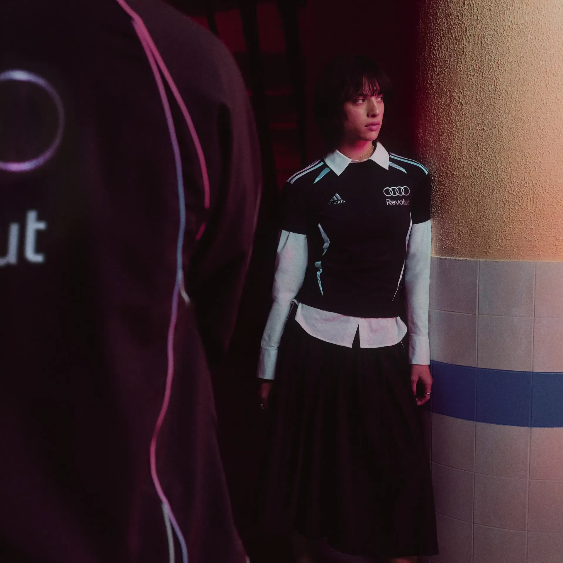 Young female model leaning against the wall wearign black adidas teamwear outfit in studio
