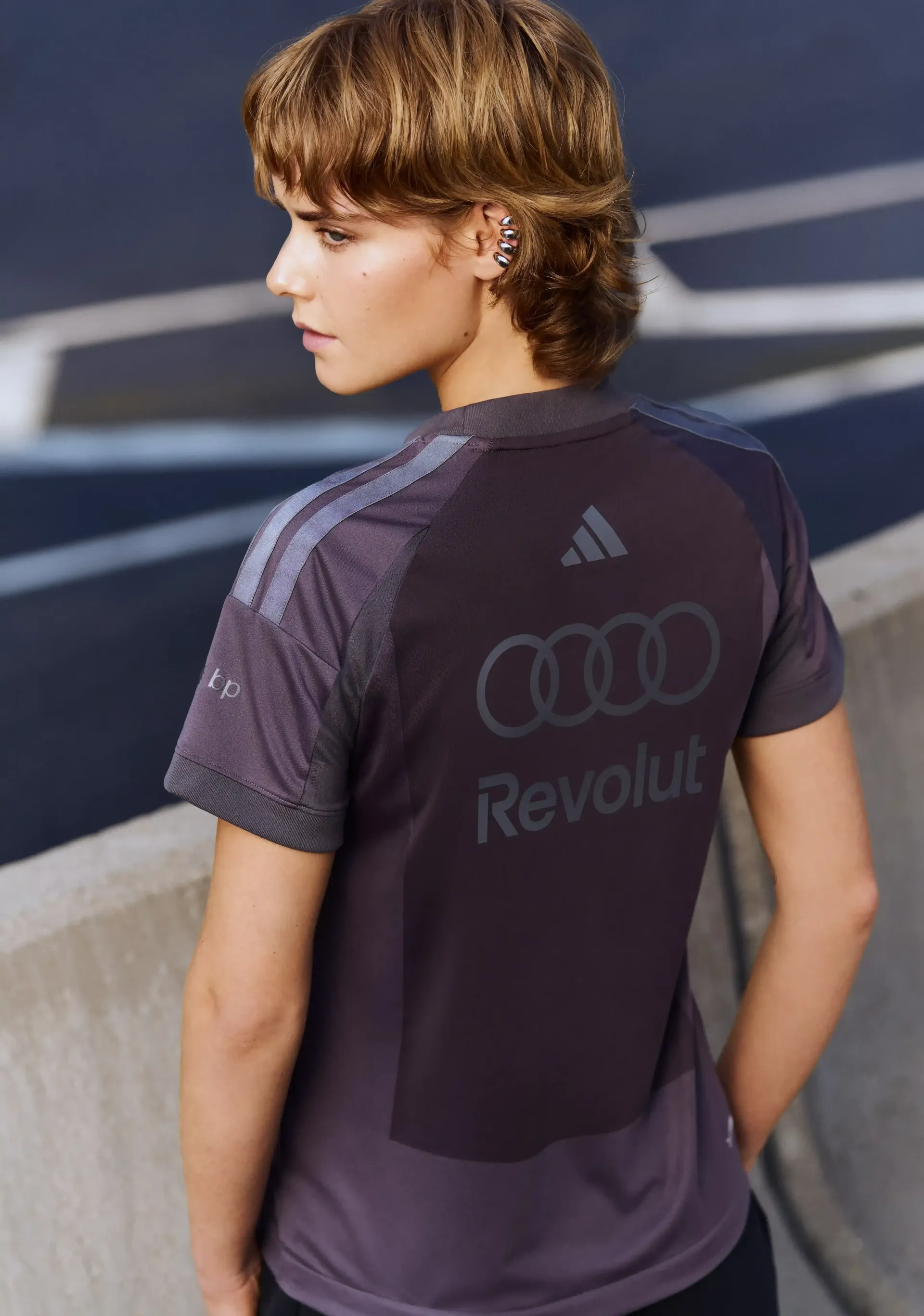 Young model in grey team short sleeve shirt back view visible branding urban background modern motorsport aesthetic