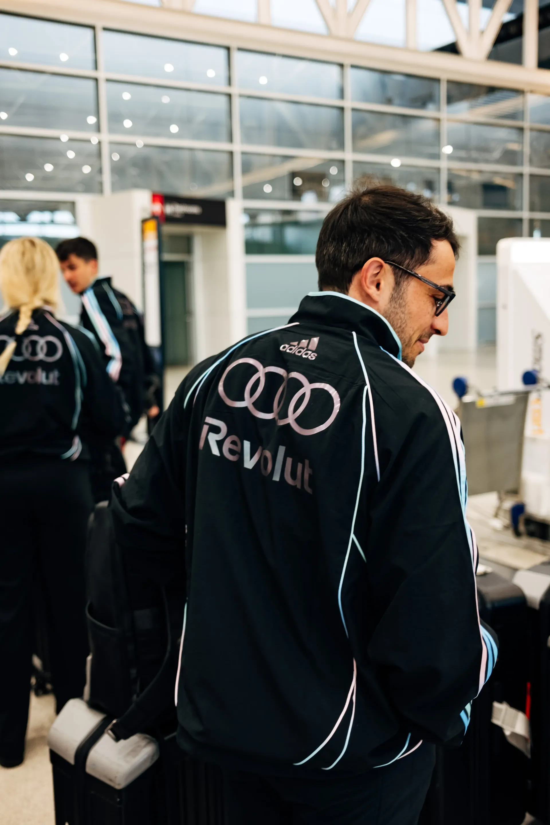 Backshot of  Audi Revolut F1®Team crew member walking through terminal corridor in the new Miami collection tracksuit.