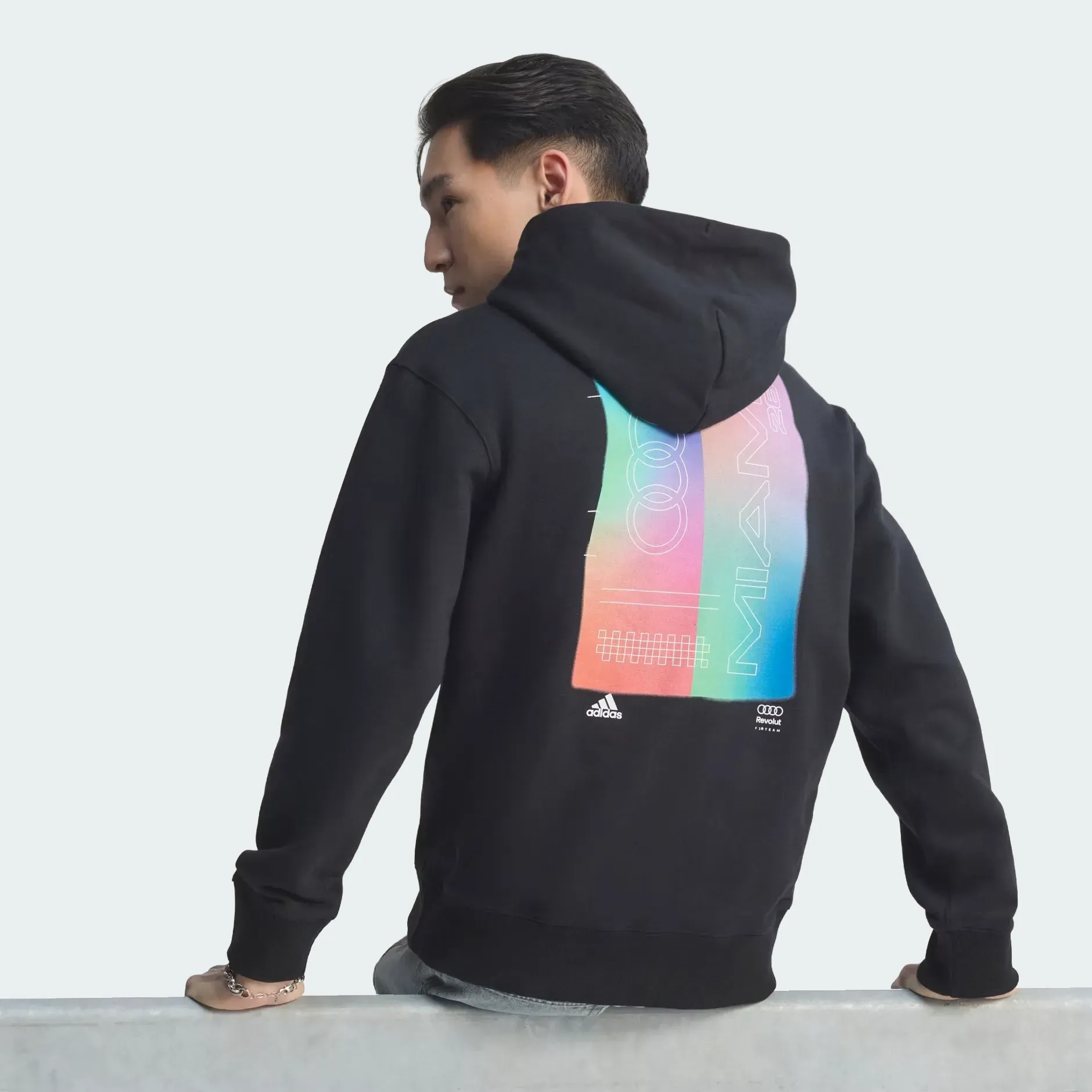 Backshot of a young male model wearing adidas Audi Revolut F1® Team Miami collection black graphic hoodie in the studio