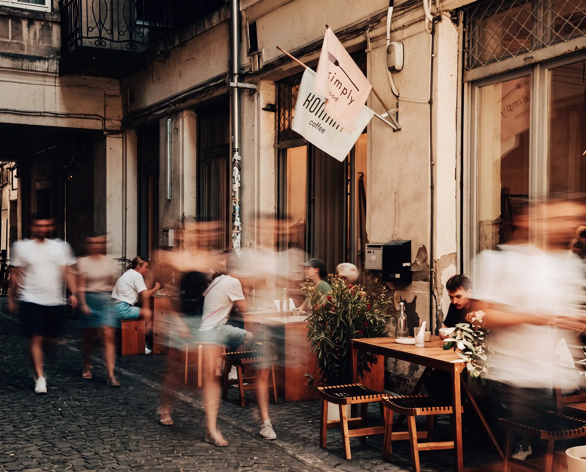 Bustling outdoor café on a historic street in Budapest with pedestrians passing by in motion blur.
