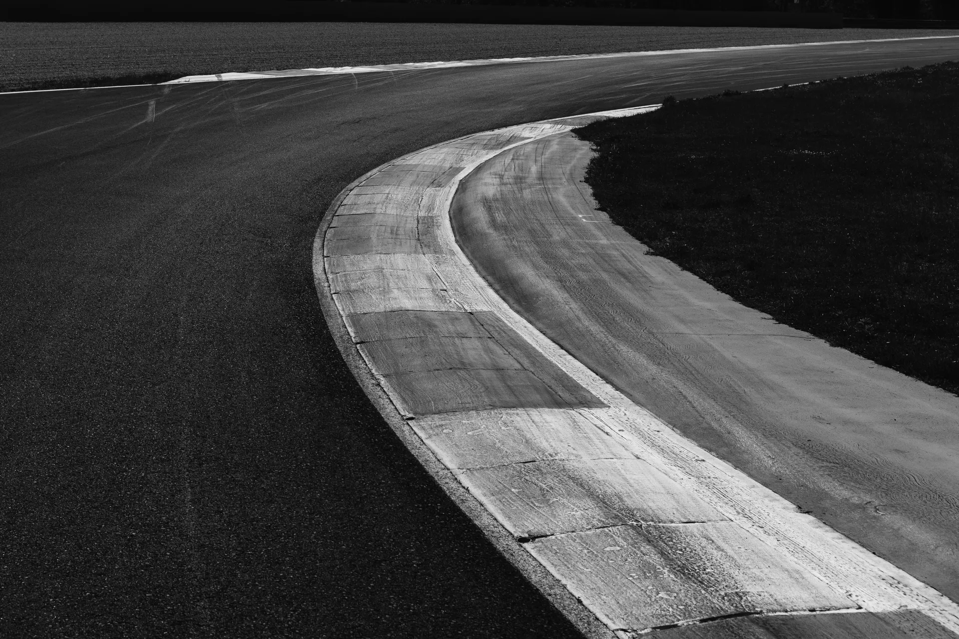 Black-and-white close-up of a racetrack corner with prominent kerbing and smooth asphalt.