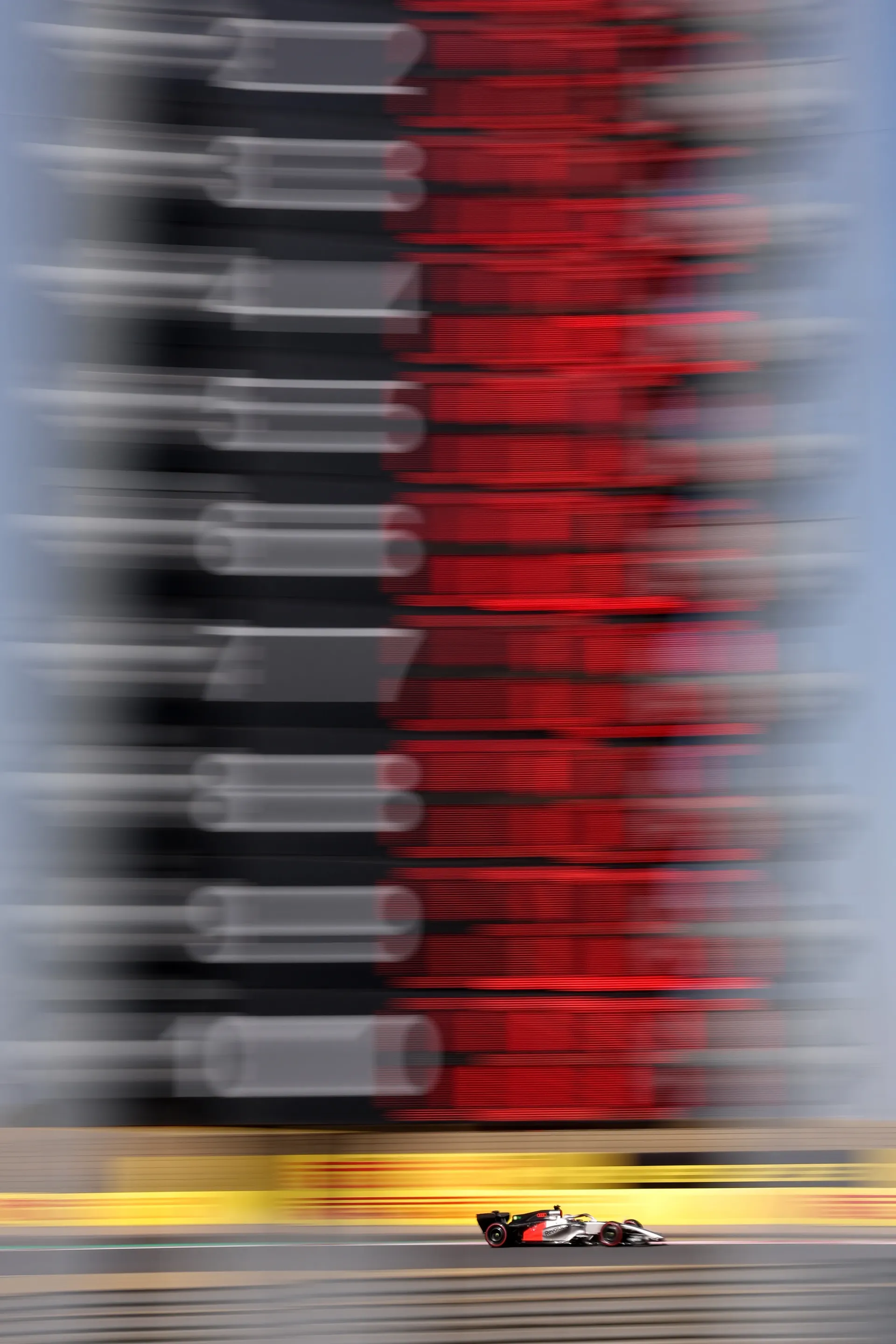 Formula 1 car racing past a grandstand with motion blur emphasizing speed and performance.