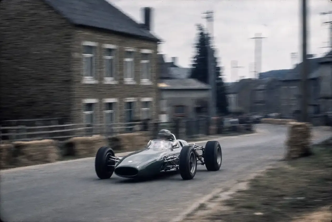 Historic Formula 1 race car driving through a village street near the Belgian Grand Prix circuit.