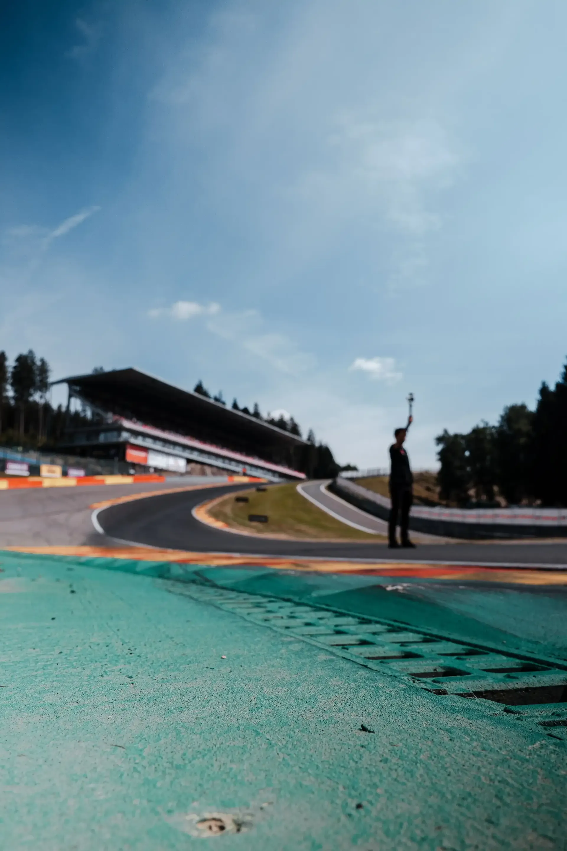 Low-angle trackside view of Spa-Francorchamps curbing with grandstands in the background.