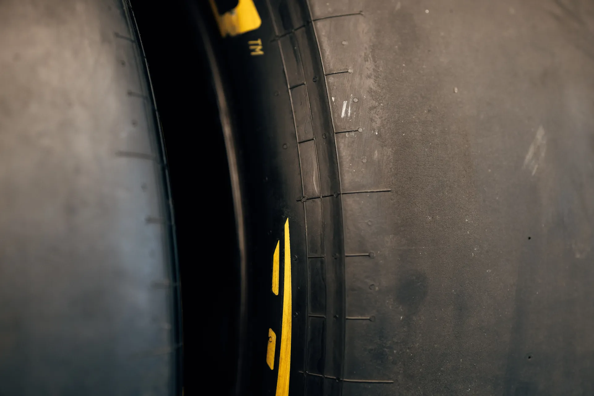 Close-up of a Formula 1 racing slick tire showing worn rubber and yellow sidewall markings.