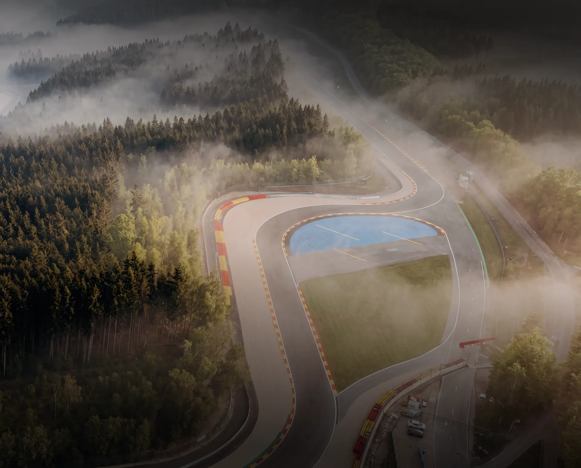 Aerial view of Eau Rouge and Raidillon at Spa-Francorchamps surrounded by misty forest.