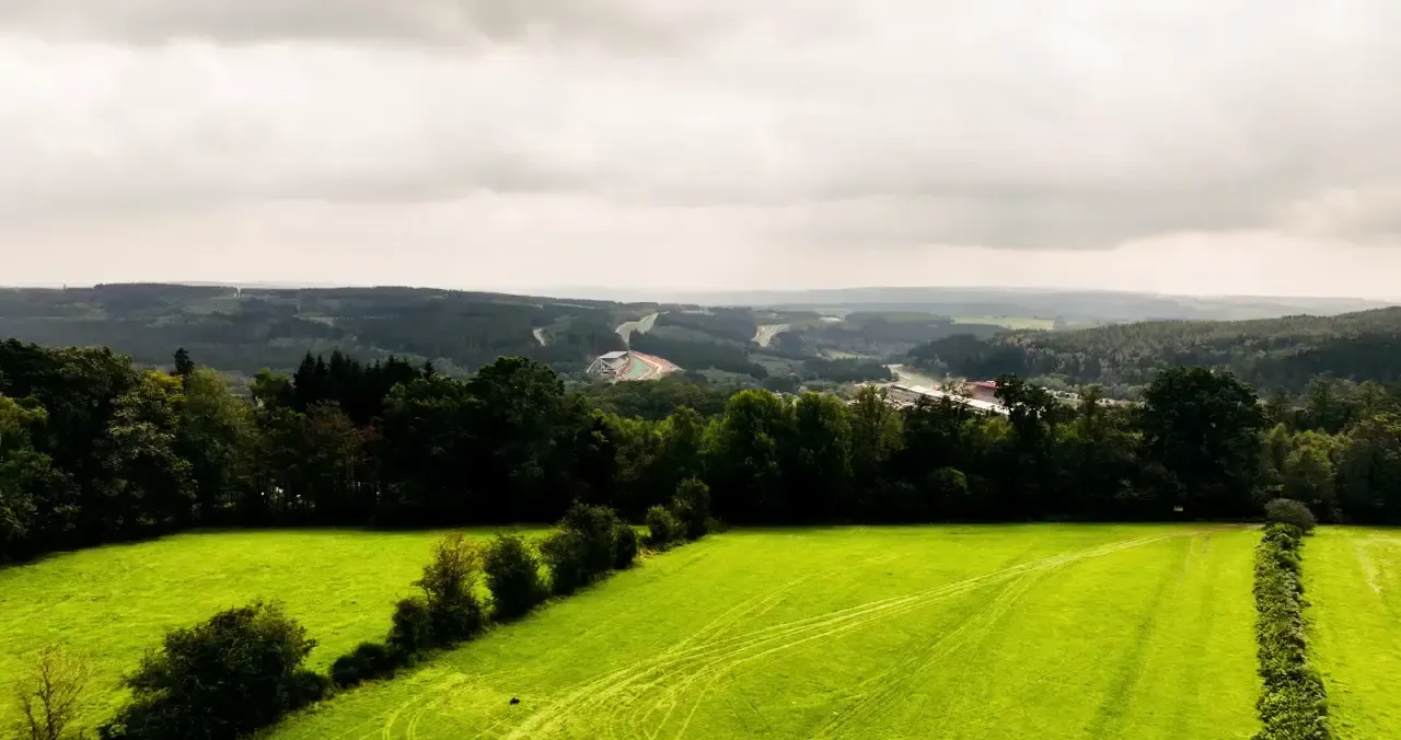 Panoramic view of the Belgian countryside with green fields overlooking the Circuit de Spa-Francorchamps in the distance.