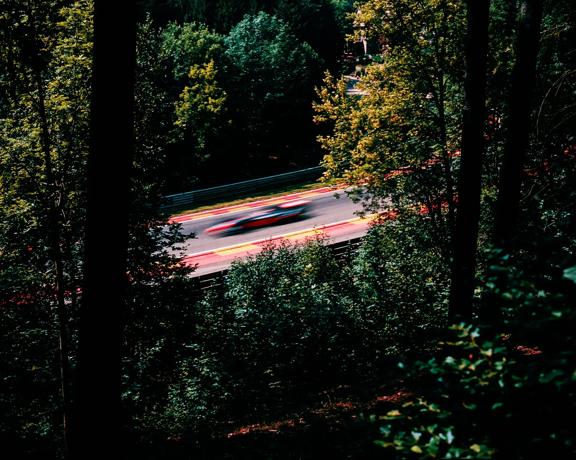 Race car light trails speeding through a forested section of Circuit de Spa-Francorchamps at dusk.