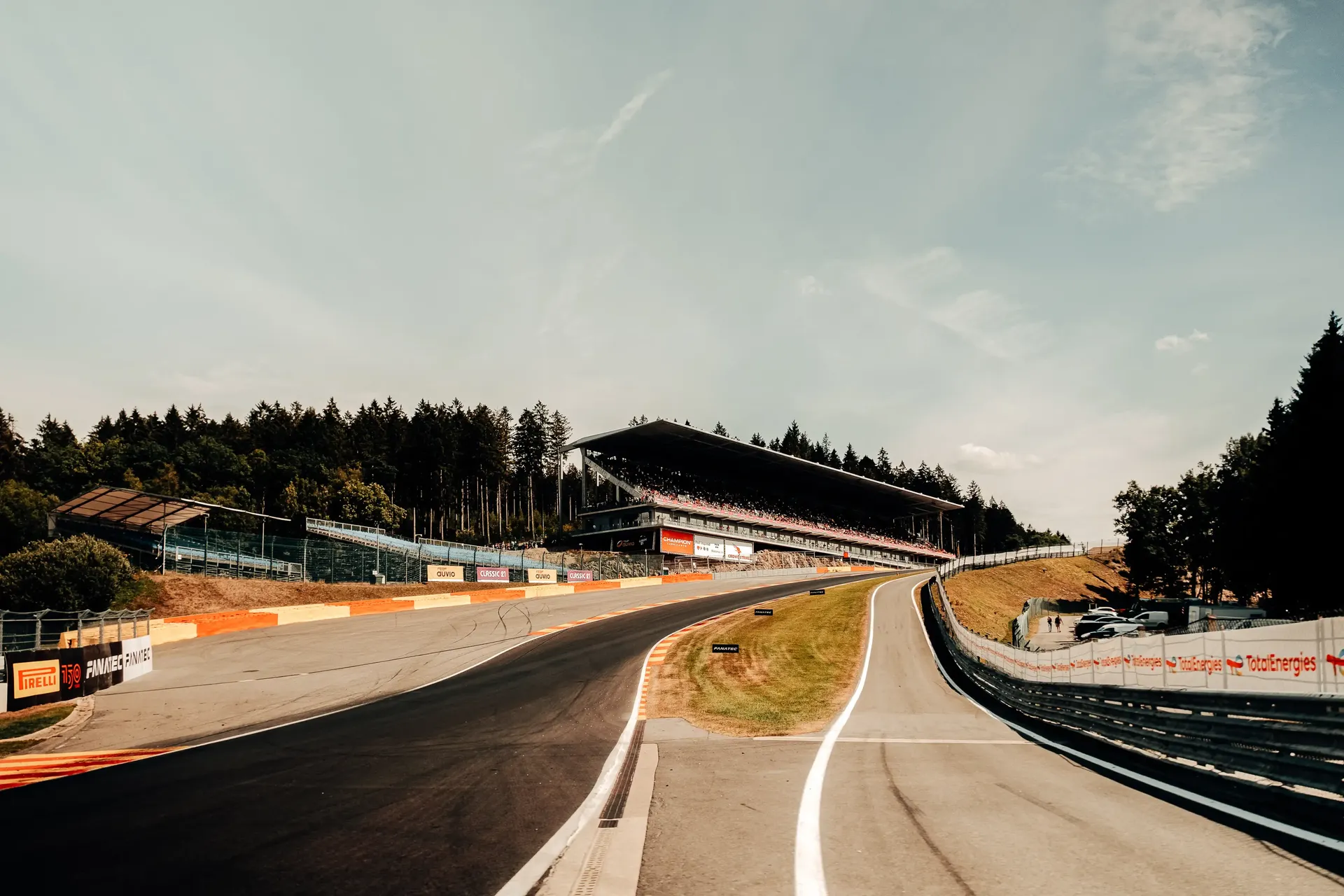 Track-level view of a sweeping section of Circuit de Spa-Francorchamps with barriers and surrounding forest.