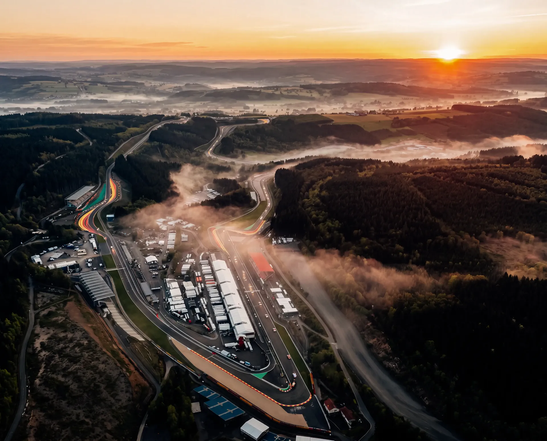 Sunrise aerial view of Circuit de Spa-Francorchamps surrounded by mist-covered forests and rolling hills.