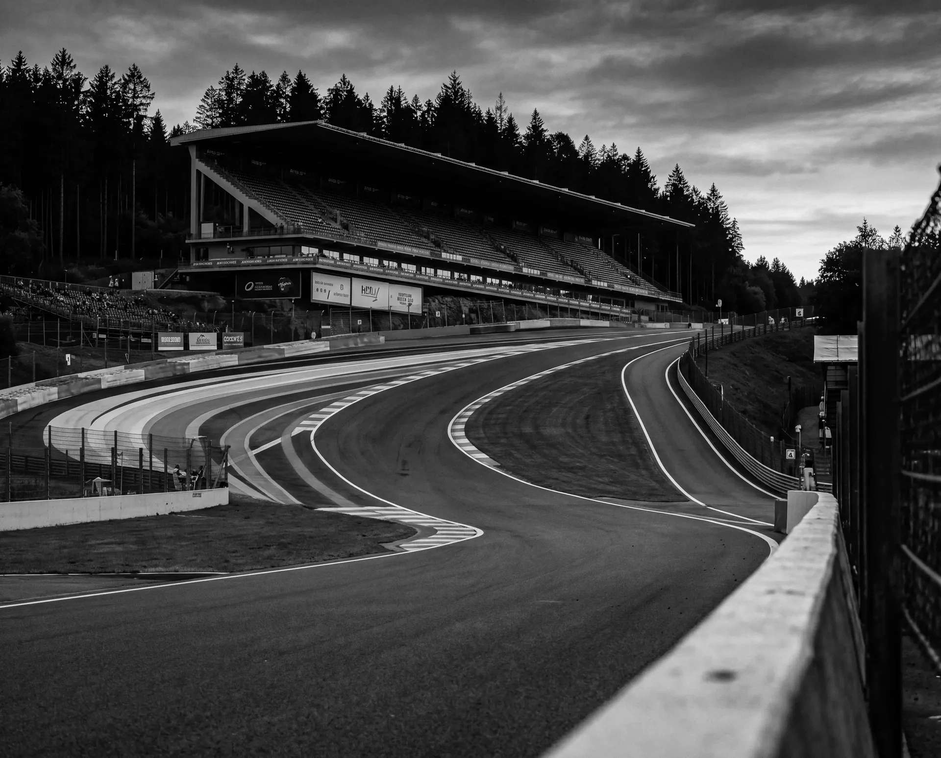 Black-and-white trackside view looking uphill through the Raidillon corner with grandstands alongside the circuit.