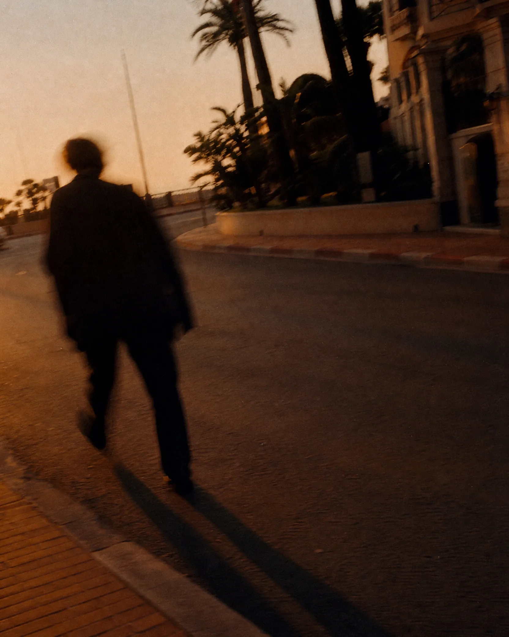 Silhouetted pedestrian crossing an open urban space in Monaco during sunset.