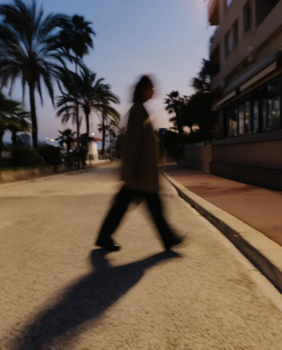 Pedestrian crossing a palm-lined promenade under bright Mediterranean sunlight.