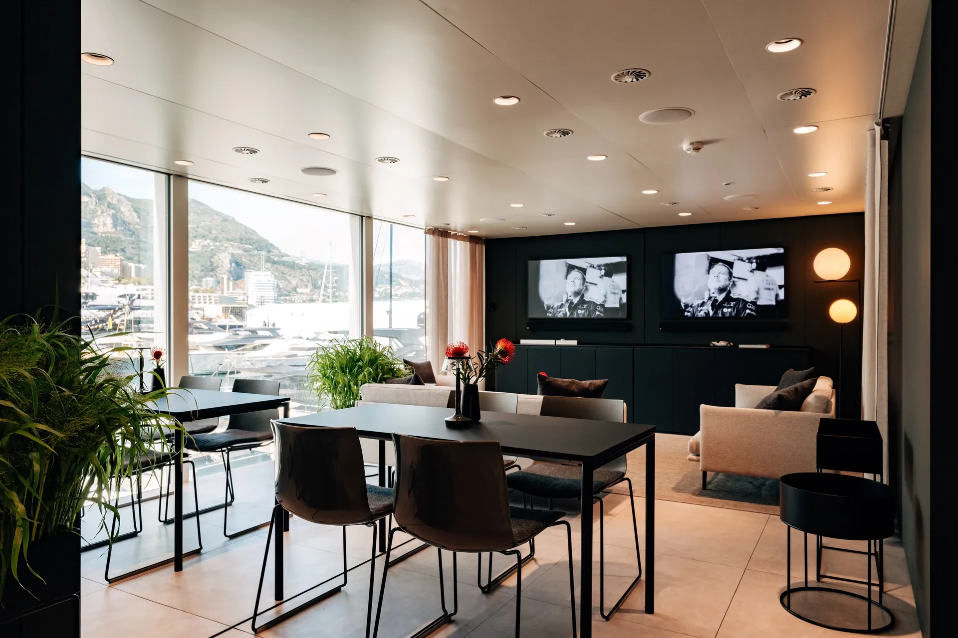 Bright hospitality lounge with seating, greenery, and paddock-facing windows.
