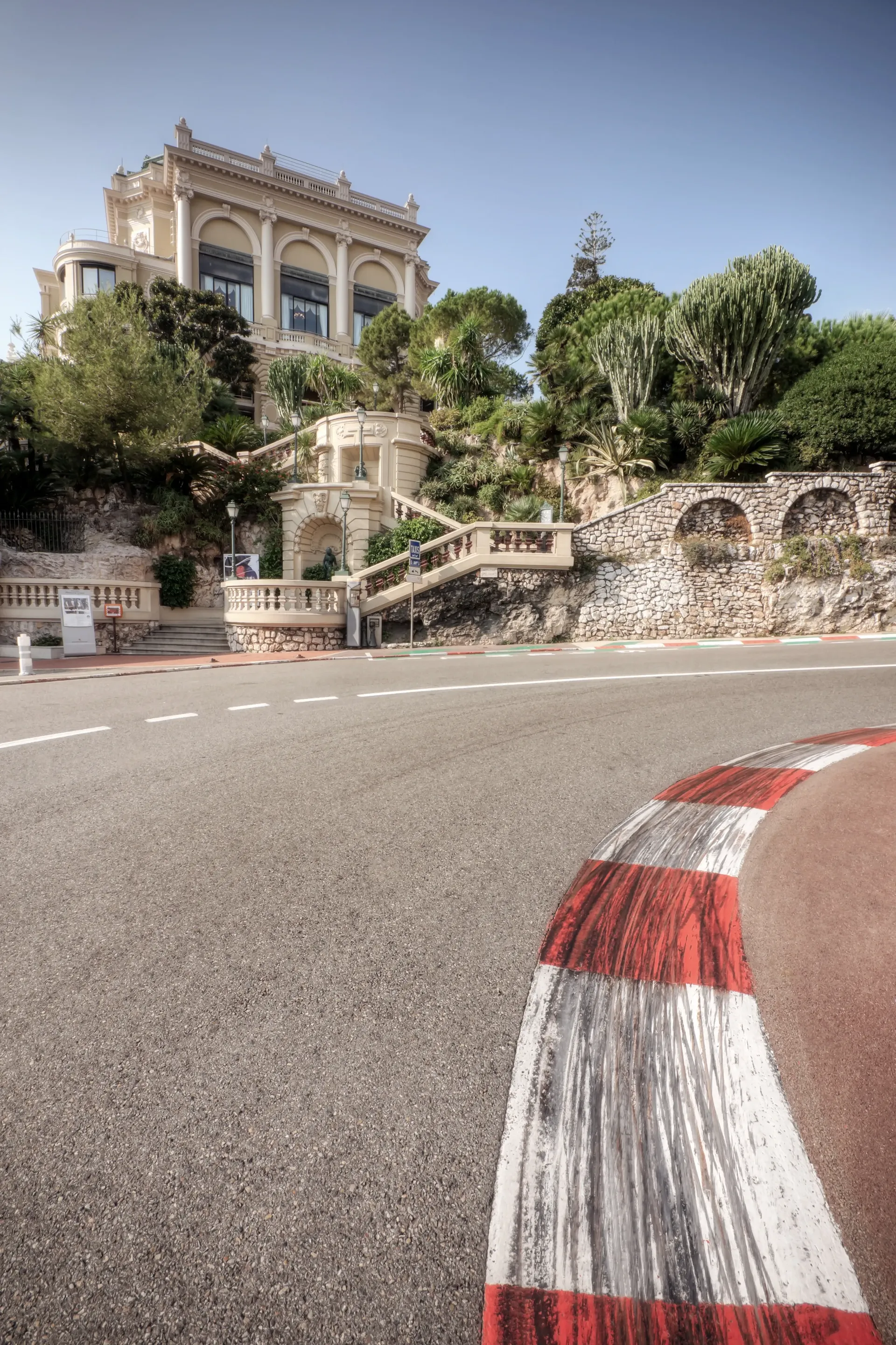 Monaco street corner with a red-and-white curb, bordered by palm trees and a historic villa.