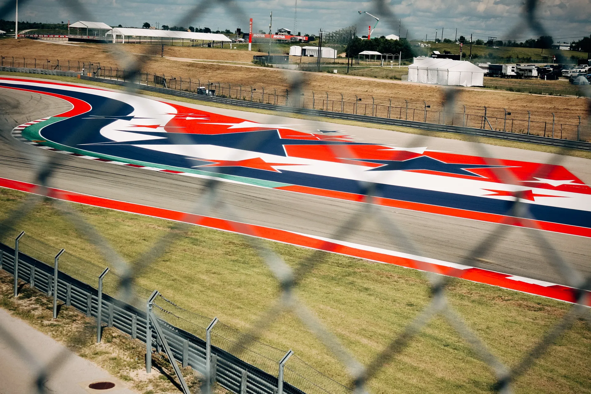 Empty street circuit curving between concrete walls and fencing, with grandstands and trees in the background.