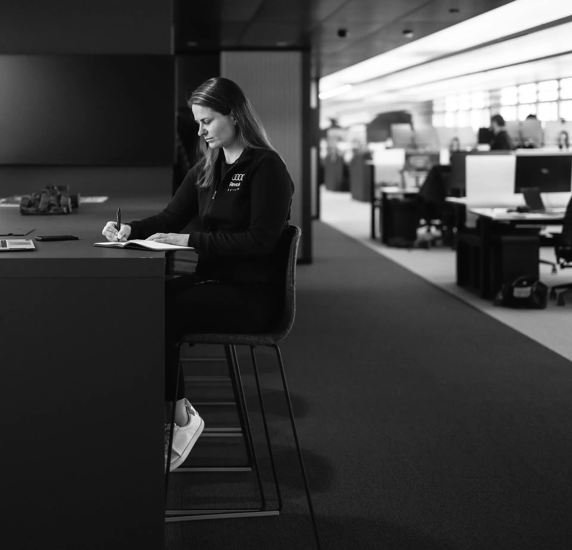 Black-and-white image of Sandra Internal communications of Audi Revolut F1® Team seated on a stool at a workstation.