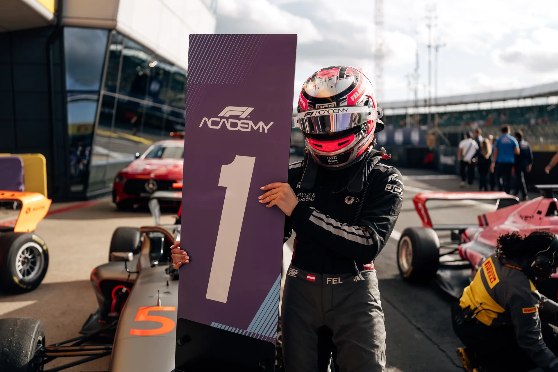 F1 Academy driver Emma Felbermayr holding a first-place podium board in parc fermé after a race victory.