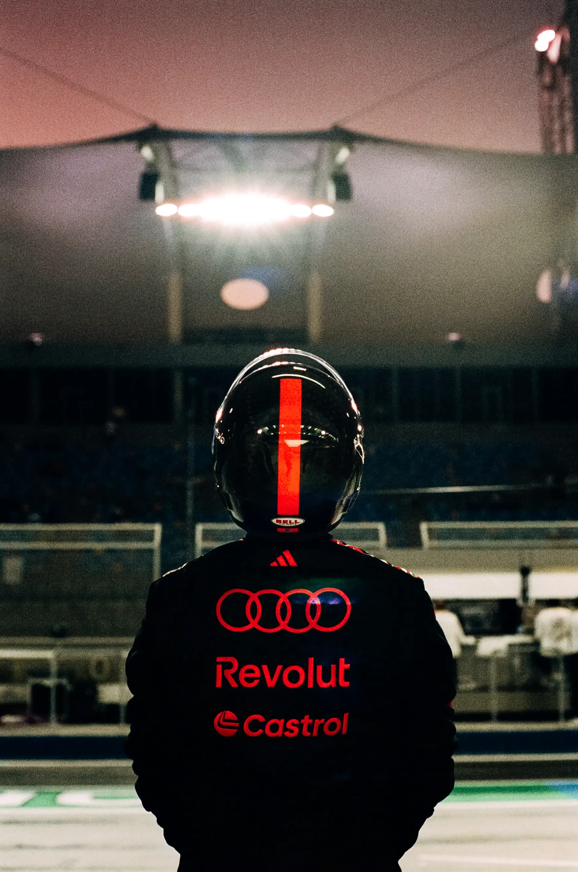 An Audi Revolut F1® Team mechanic stands in the pit lane overlooking the circuit at night.
