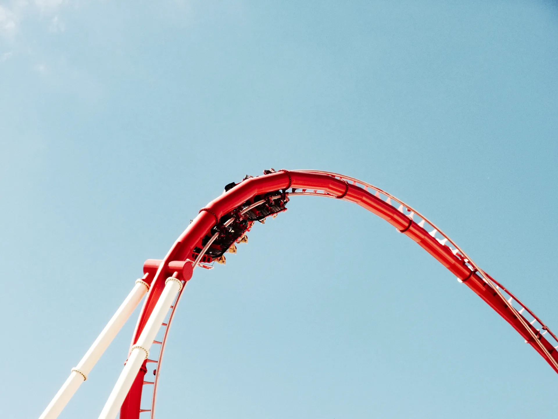 Red roller coaster track arching against a clear blue sky