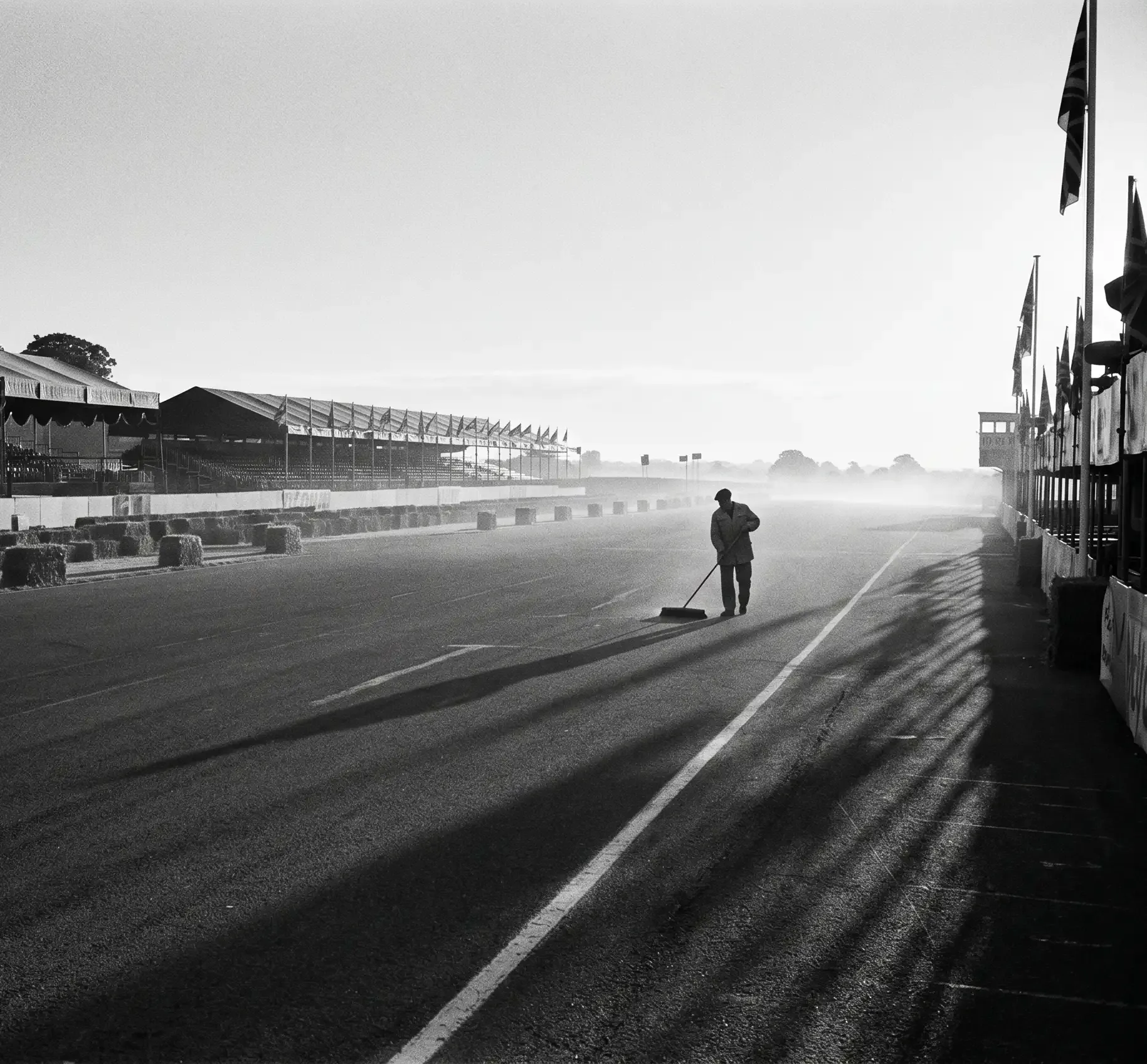 Black-and-white image of a lone figure walking along the Silverstone pit lane at sunrise.