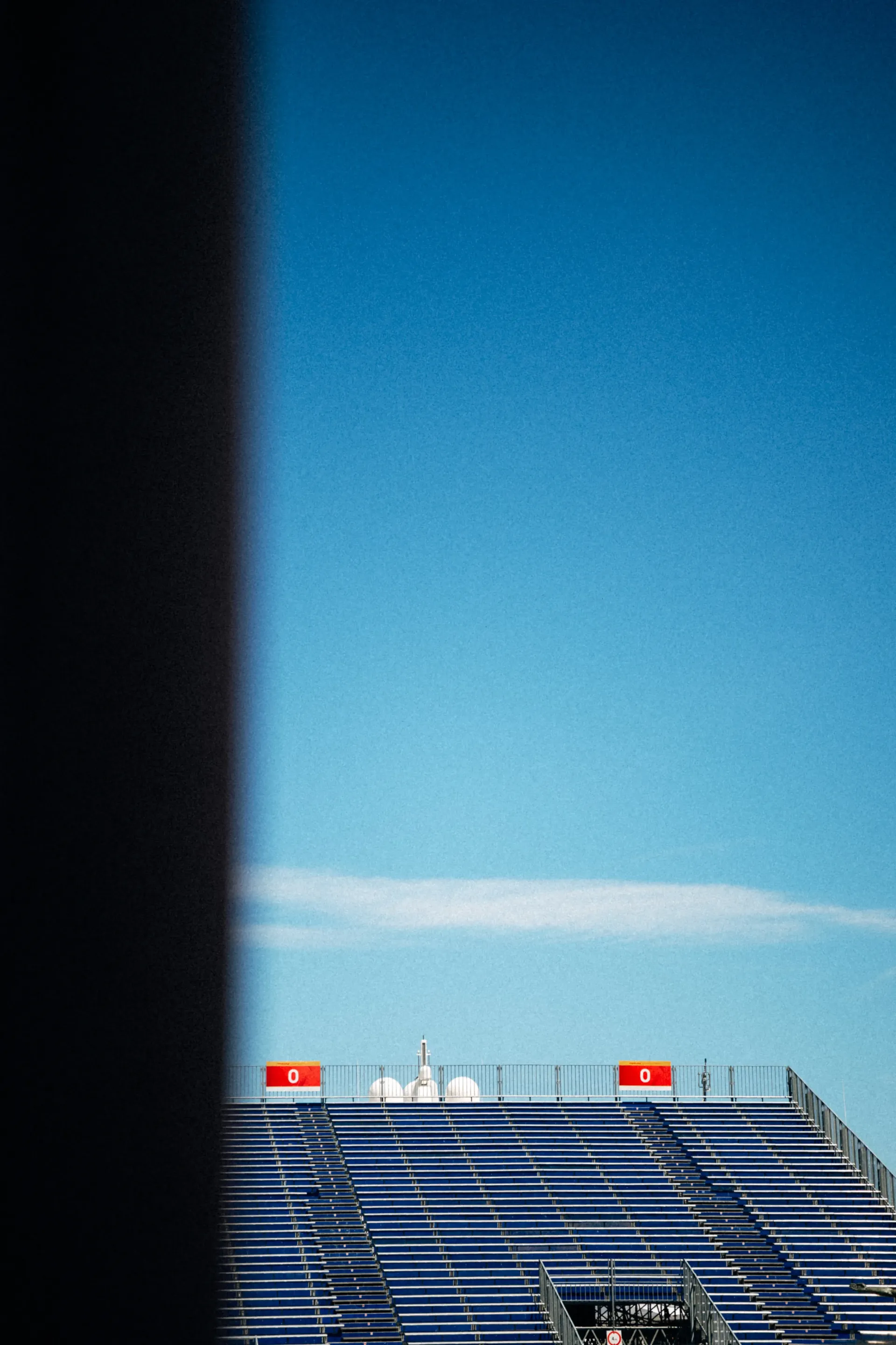 View through a dark gap onto an empty race track grandstand in sunlight
