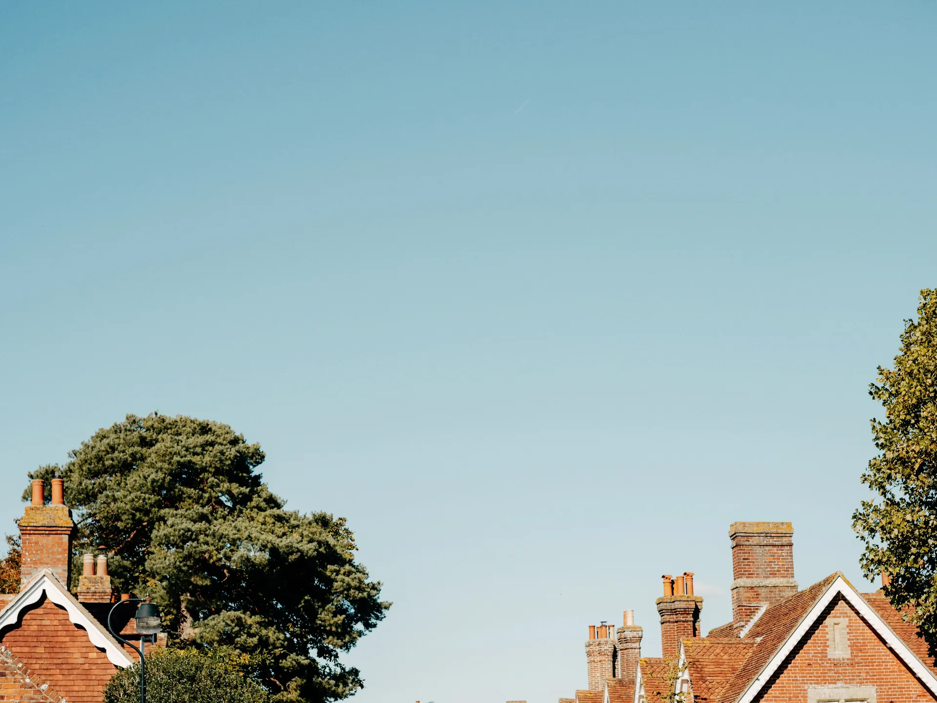 Tree-lined residential street with traditional English houses under a clear blue sky.