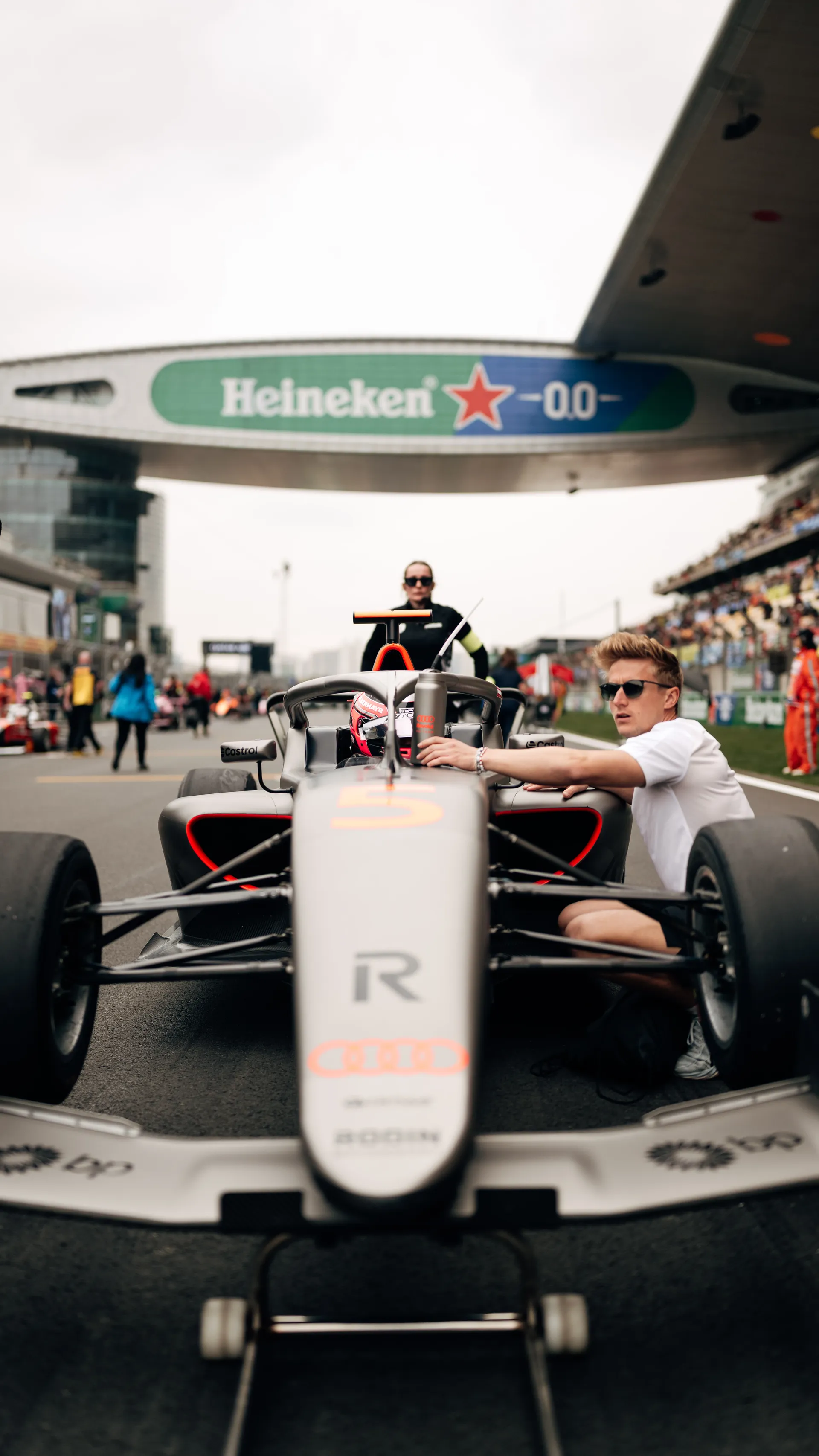 Emma Felbermayr sits in her F1 Academy car on the Shanghai starting grid while a team member kneels beside the cockpit before the race.