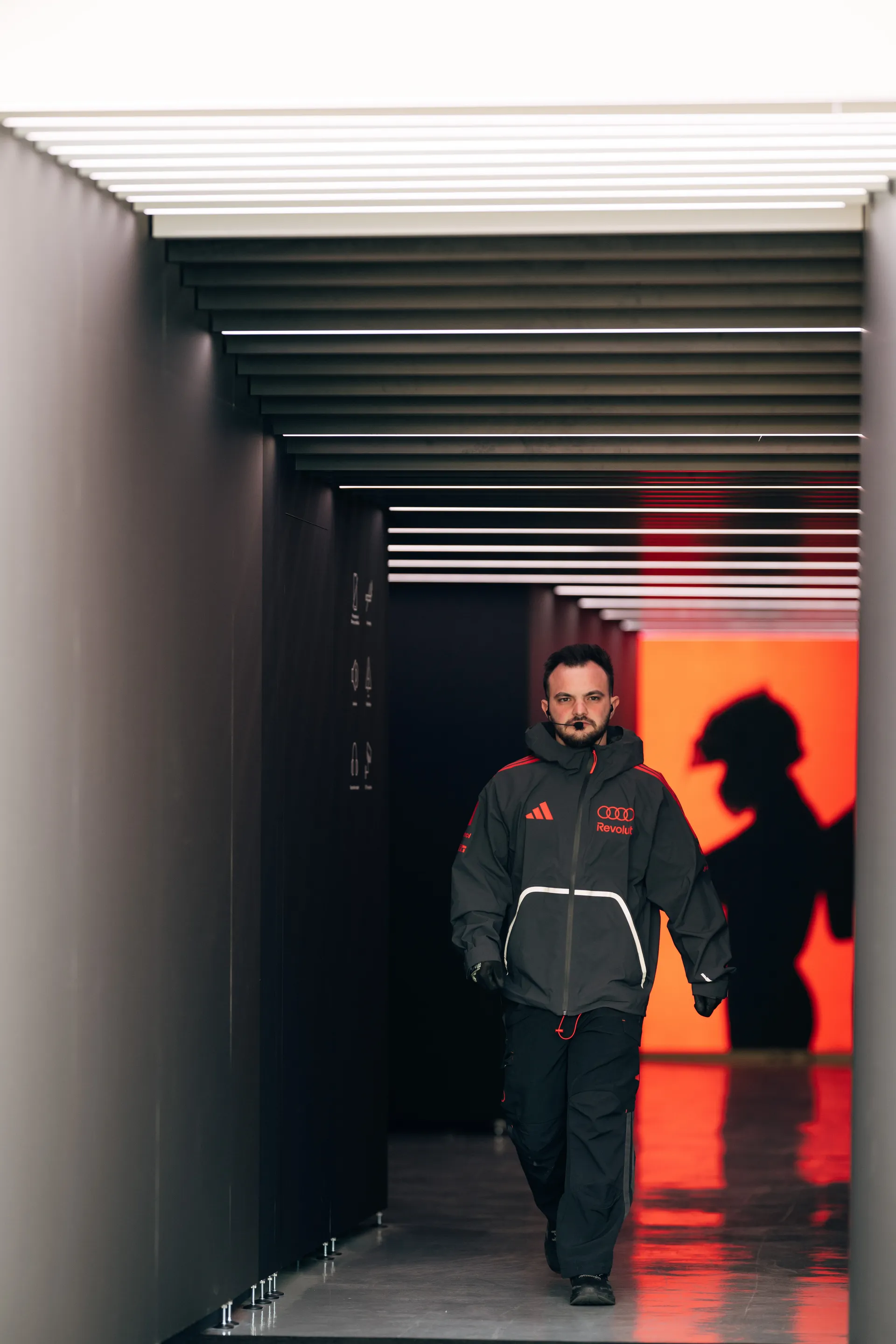 An Audi Revolut F1® Team crew member walks through the garage tunnel in Shanghai, with dramatic red light and shadow in the background.